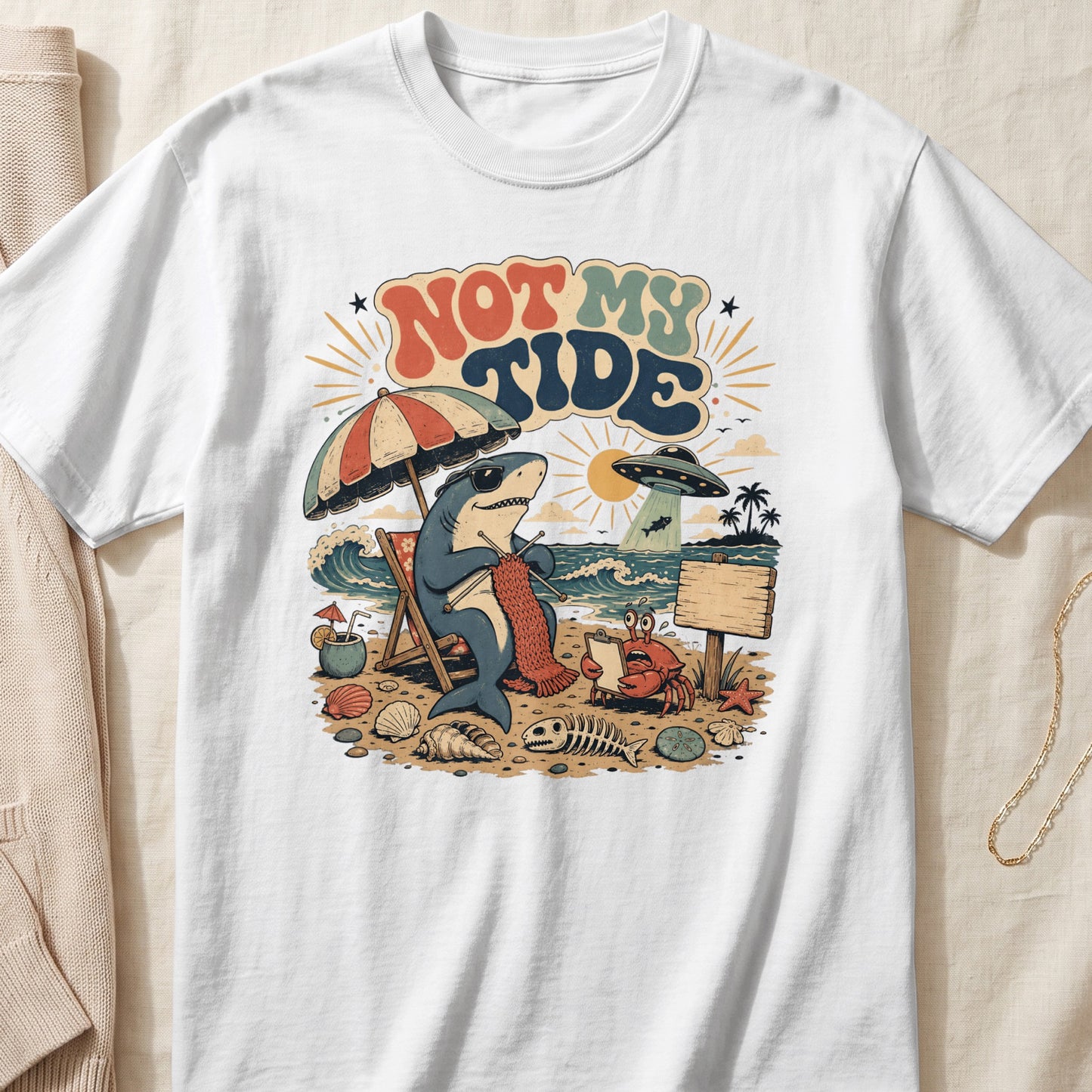 Shark knitting on a beach chair with "Not My Tide" text, UFO, and crab.