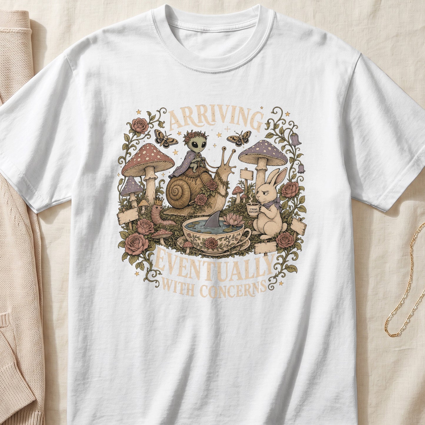 White t-shirt with a fantasy woodland graphic and text "ARRIVING EVENTUALLY WITH CONCERNS".