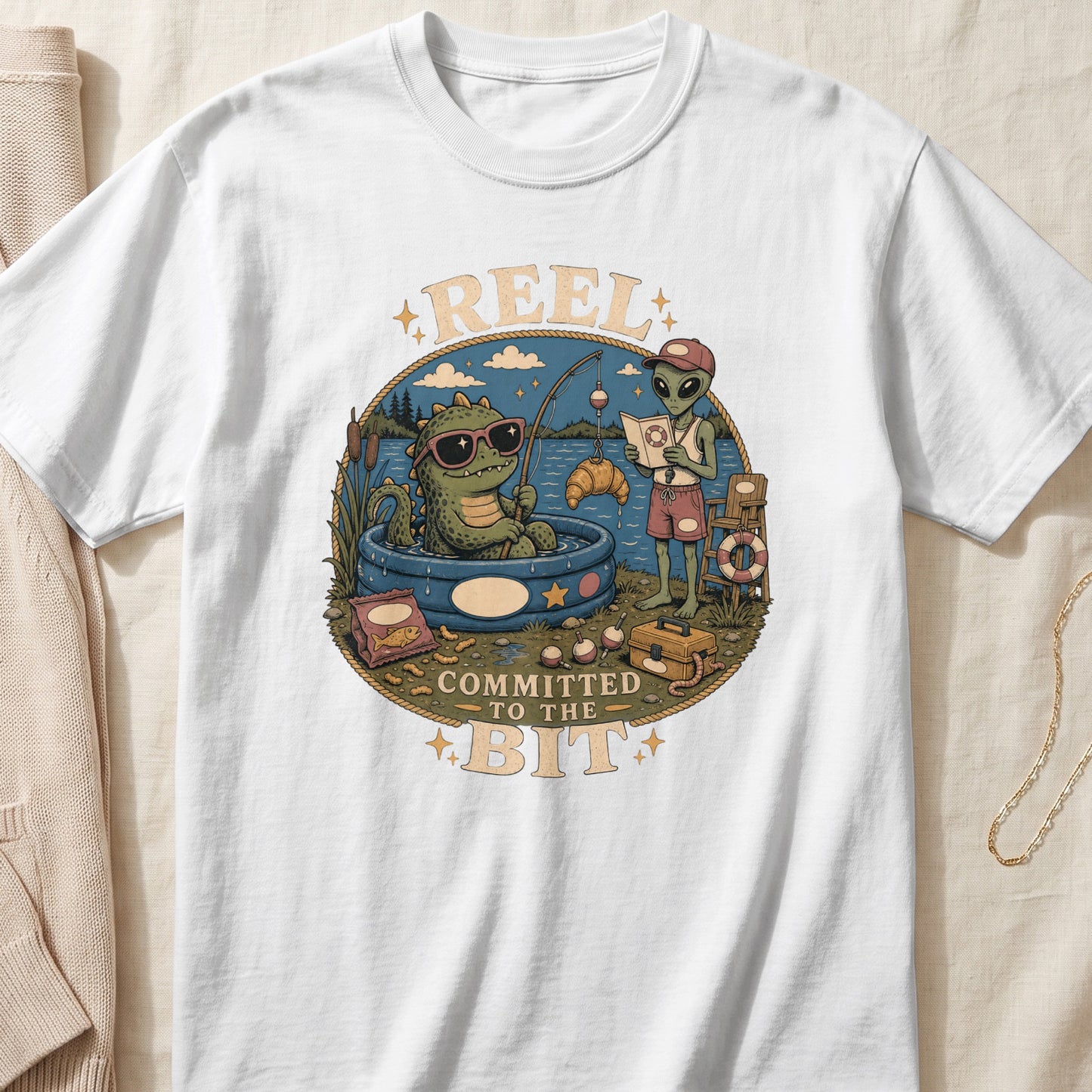 Graphic t-shirt with a cartoon of a dinosaur and an alien fishing, text reads "REEL COMMITTED TO THE BIT".