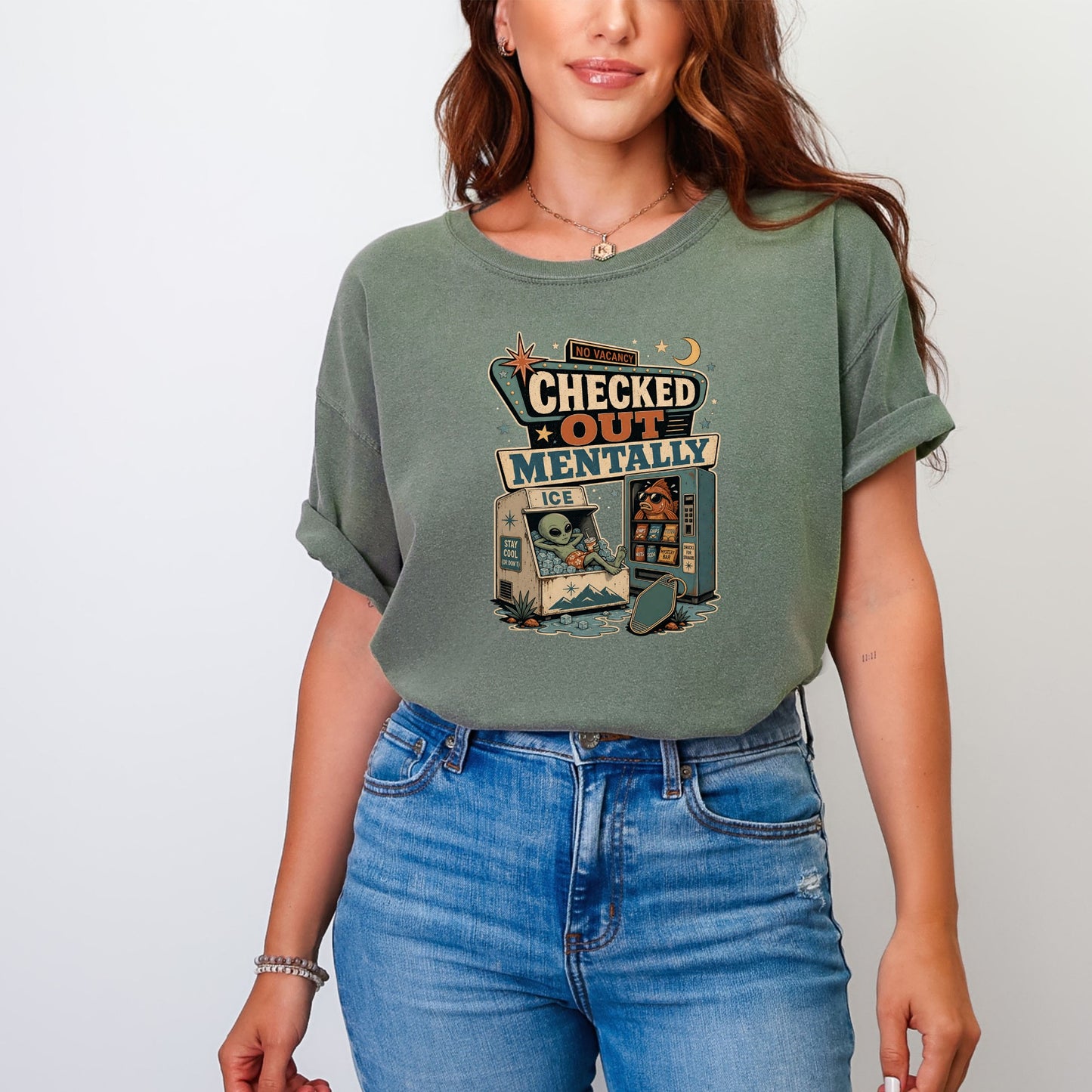 Green t-shirt graphic with "Checked Out Mentally" text, alien in ice cooler, and fish at vending machine.