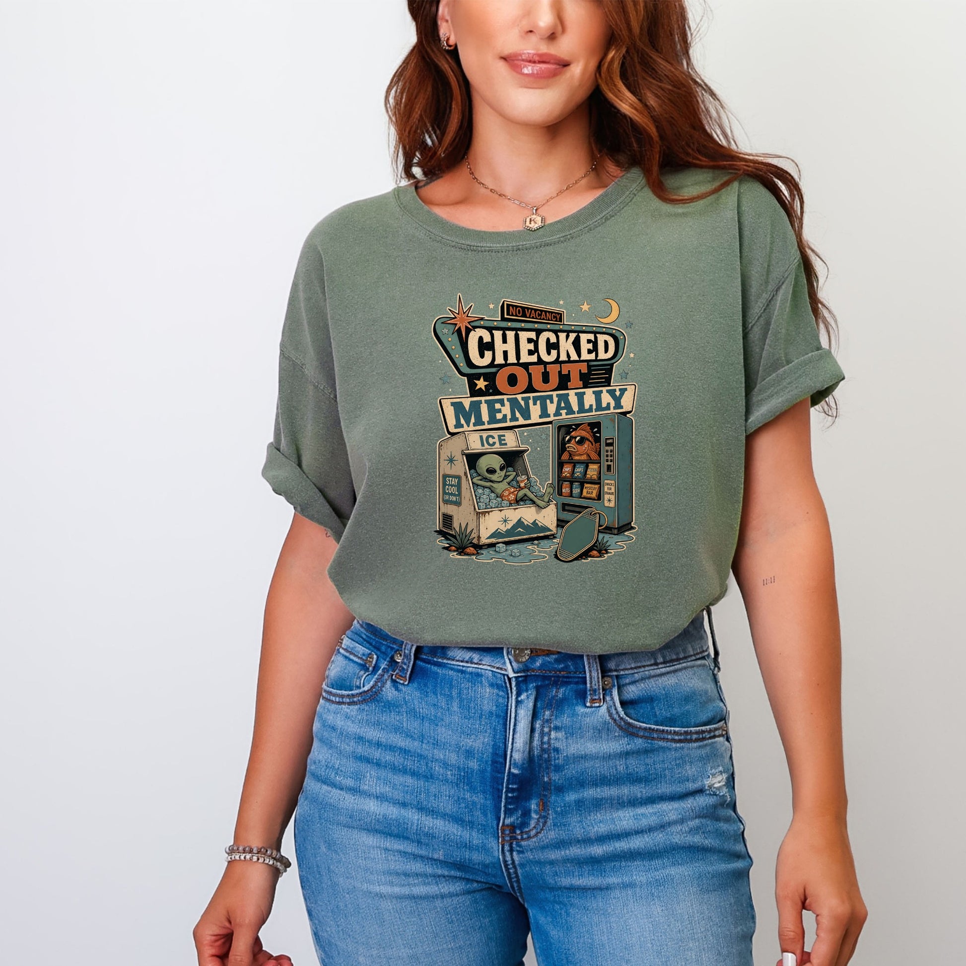Green t-shirt graphic with "Checked Out Mentally" text, alien in ice cooler, and fish at vending machine.