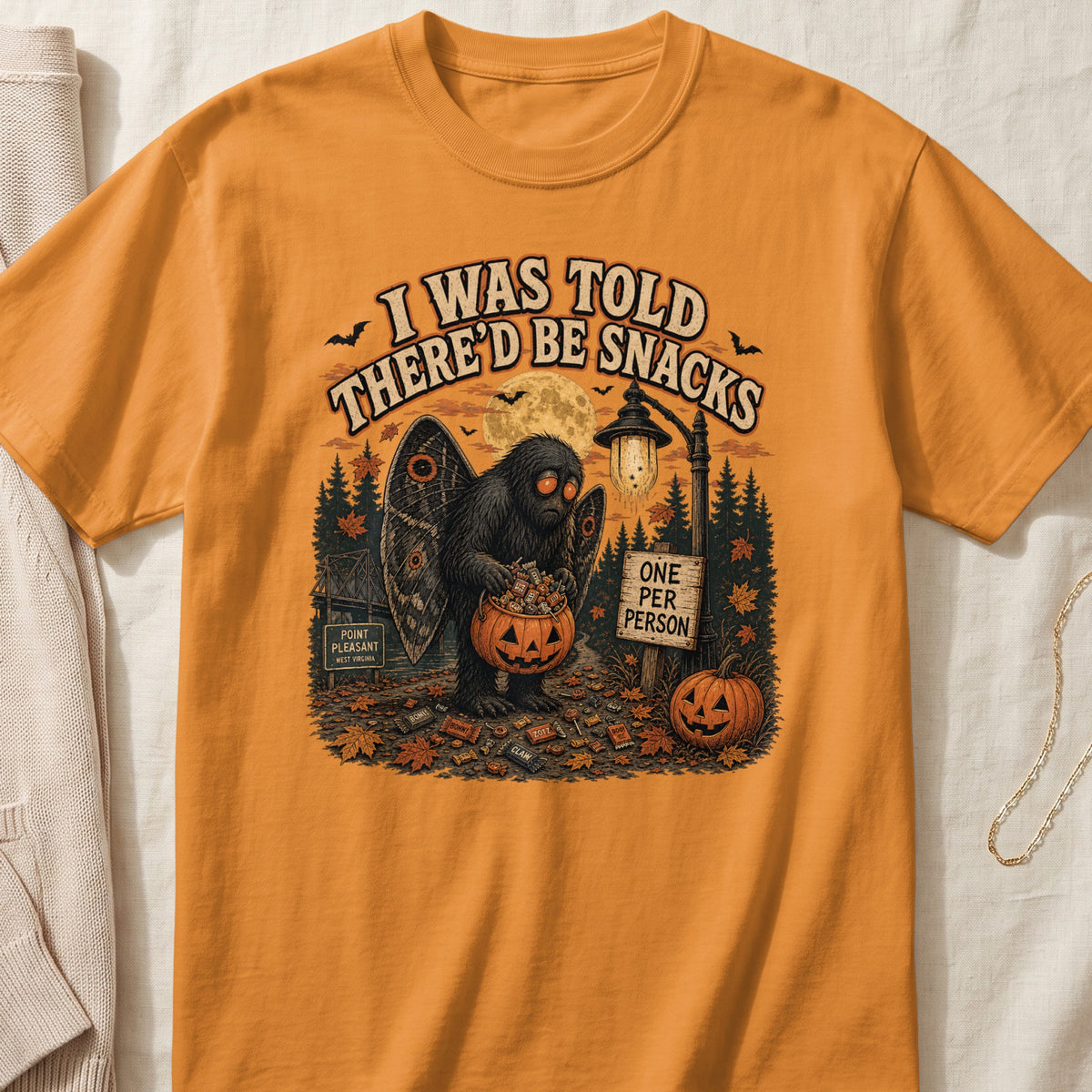 Orange t-shirt with "I Was Told There'd Be Snacks" graphic featuring Mothman holding candy.