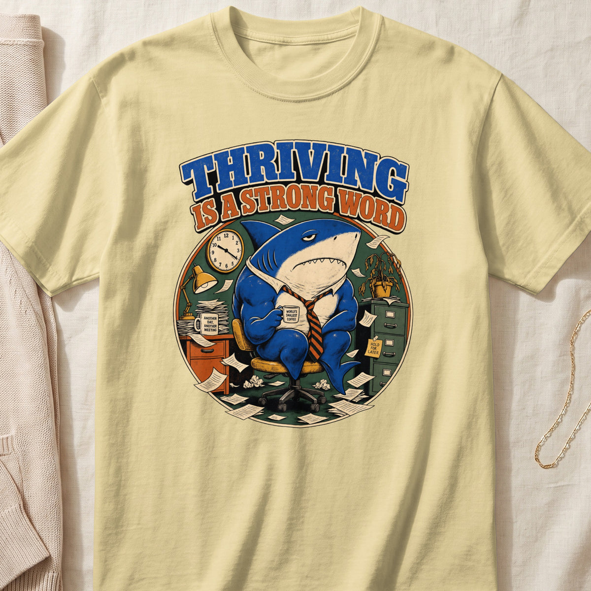 T-shirt graphic of a shark in a suit holding coffee with text "THRIVING IS A STRONG WORD".