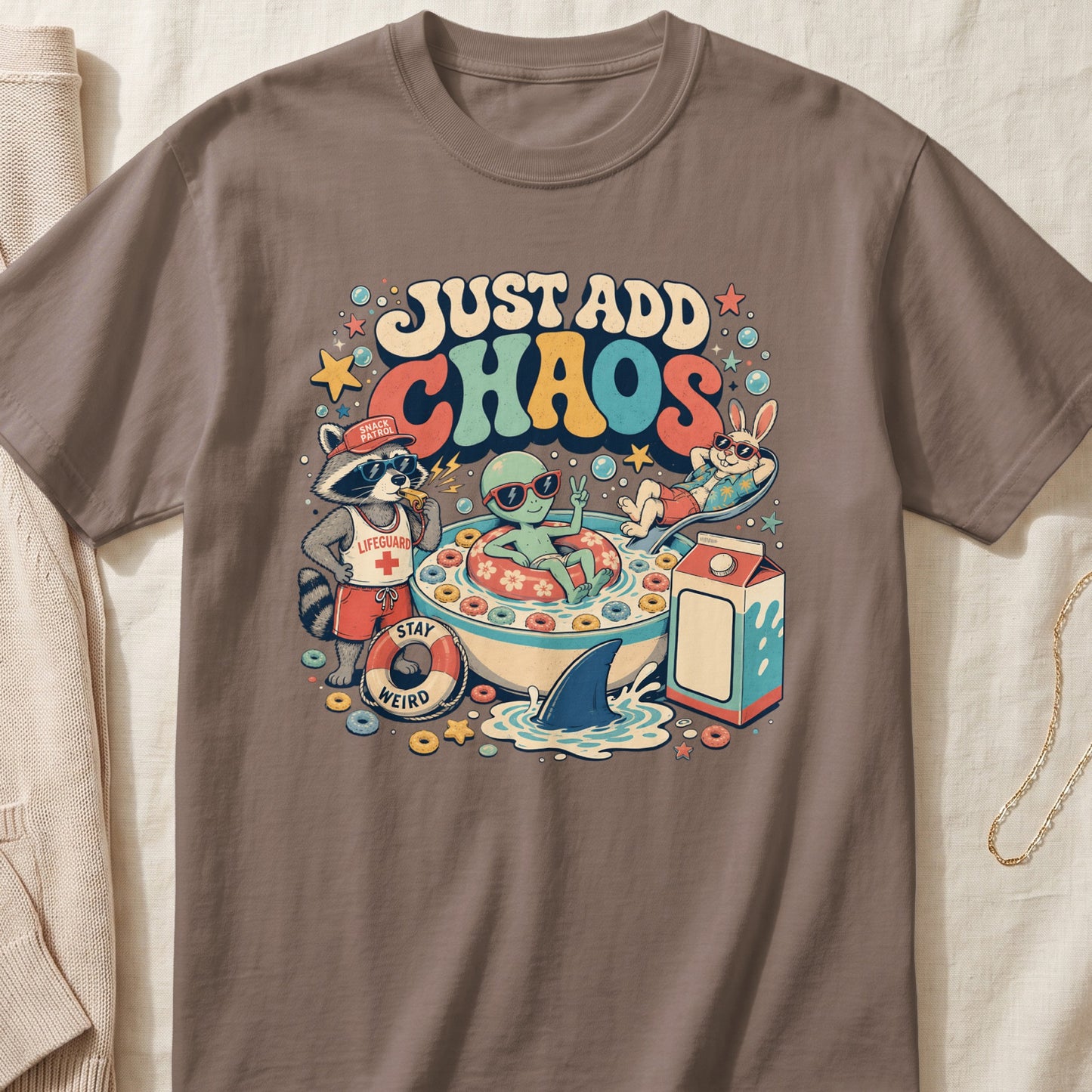 Brown crewneck t-shirt featuring a cartoon graphic of an alien and animals in a cereal bowl with the text Just Add Chaos.