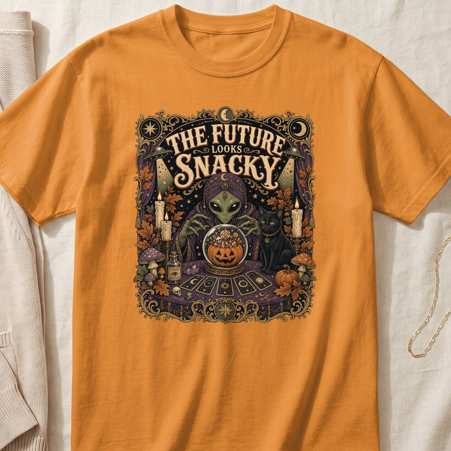 Orange t-shirt with "The Future Looks Snacky" alien fortune teller and black cat graphic.