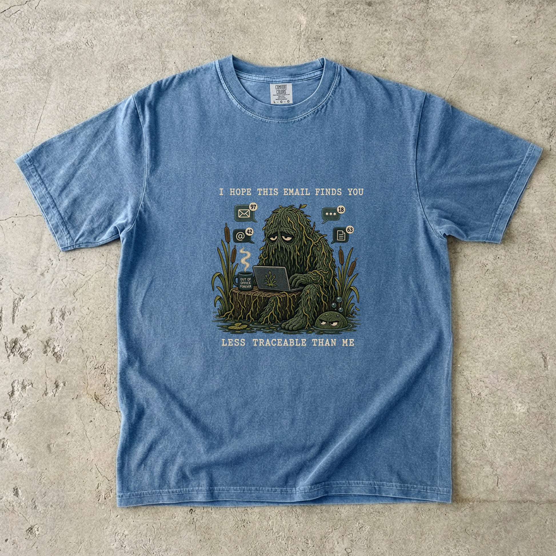 Blue t-shirt graphic of a swamp monster with a laptop and email notifications.