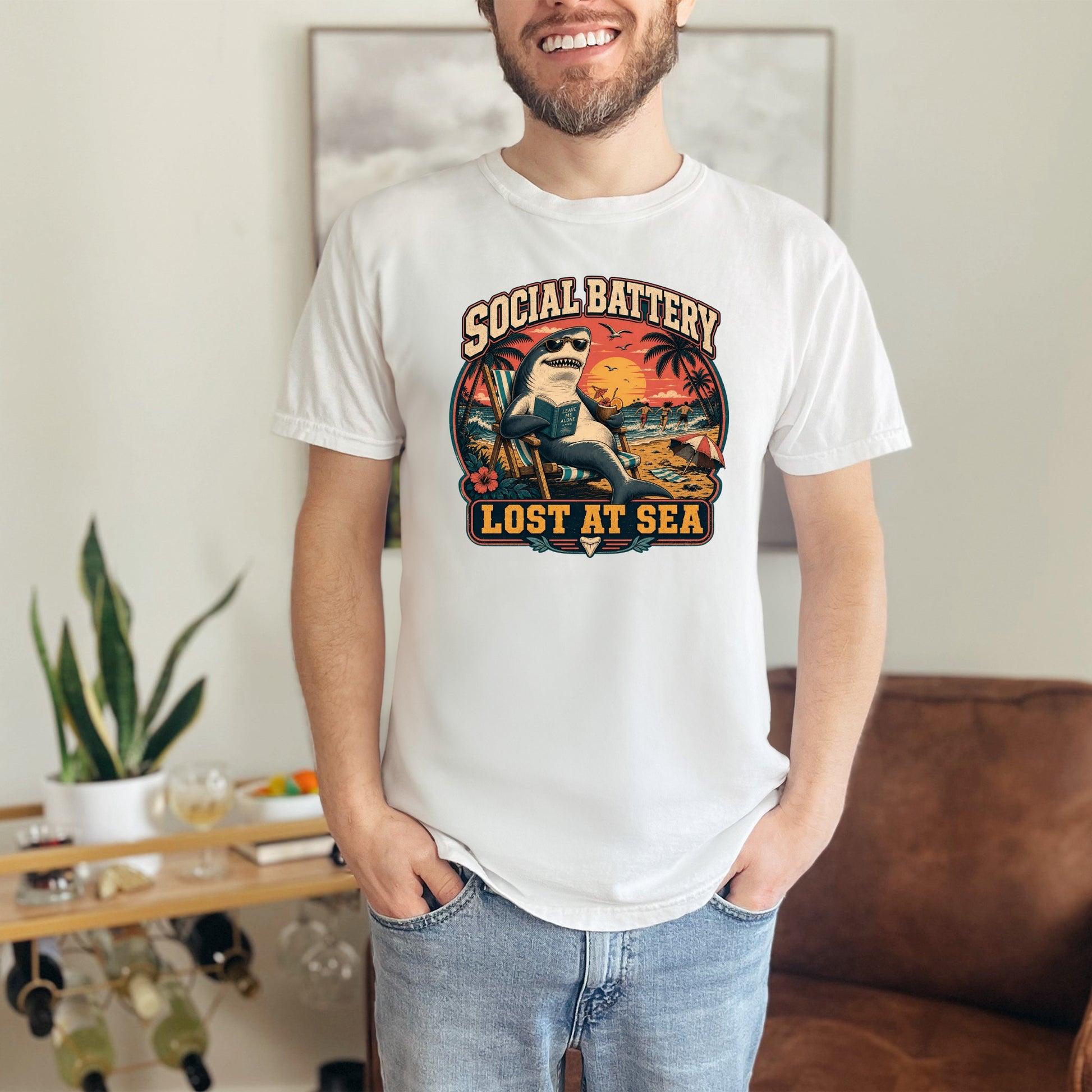 White t-shirt graphic with shark reading "Social Battery Lost at Sea" on beach scene.