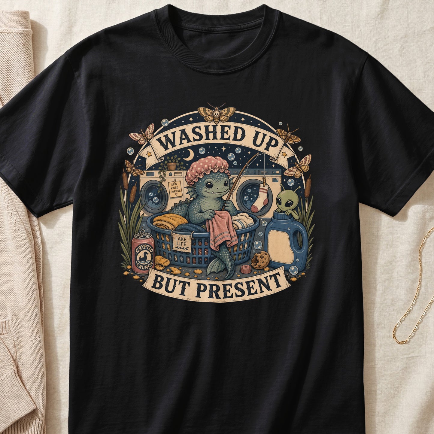 Black t-shirt with "Washed Up But Present" text and swamp creature laundry scene.