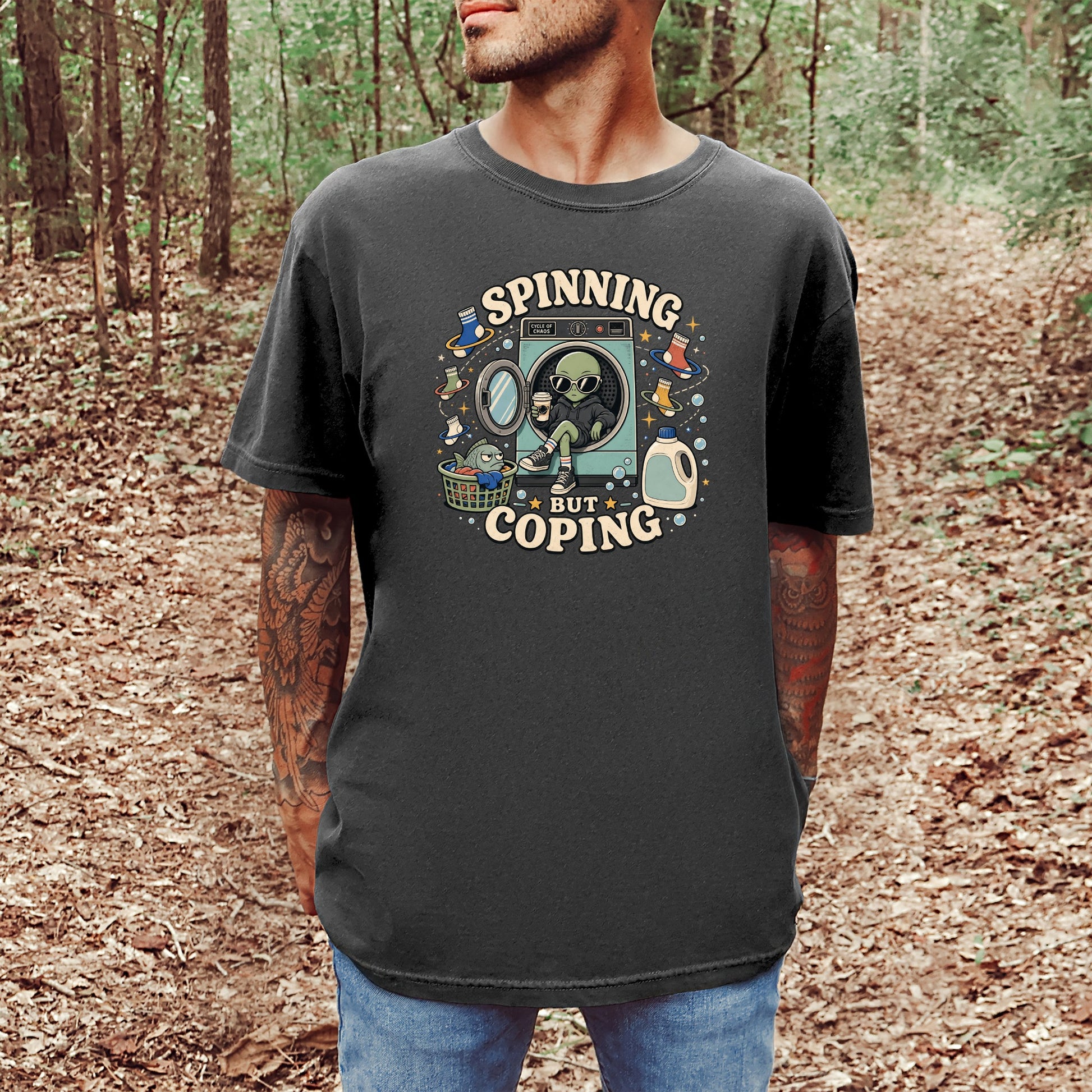Dark t-shirt graphic with text "SPINNING BUT COPING" and alien by washing machine.