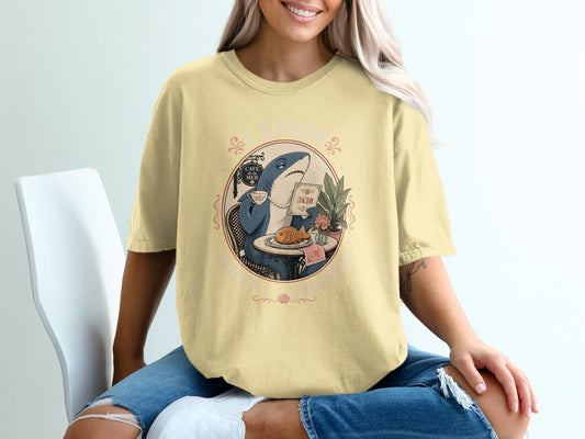 Yellow t-shirt with graphic of a shark at a cafe table reading a menu.