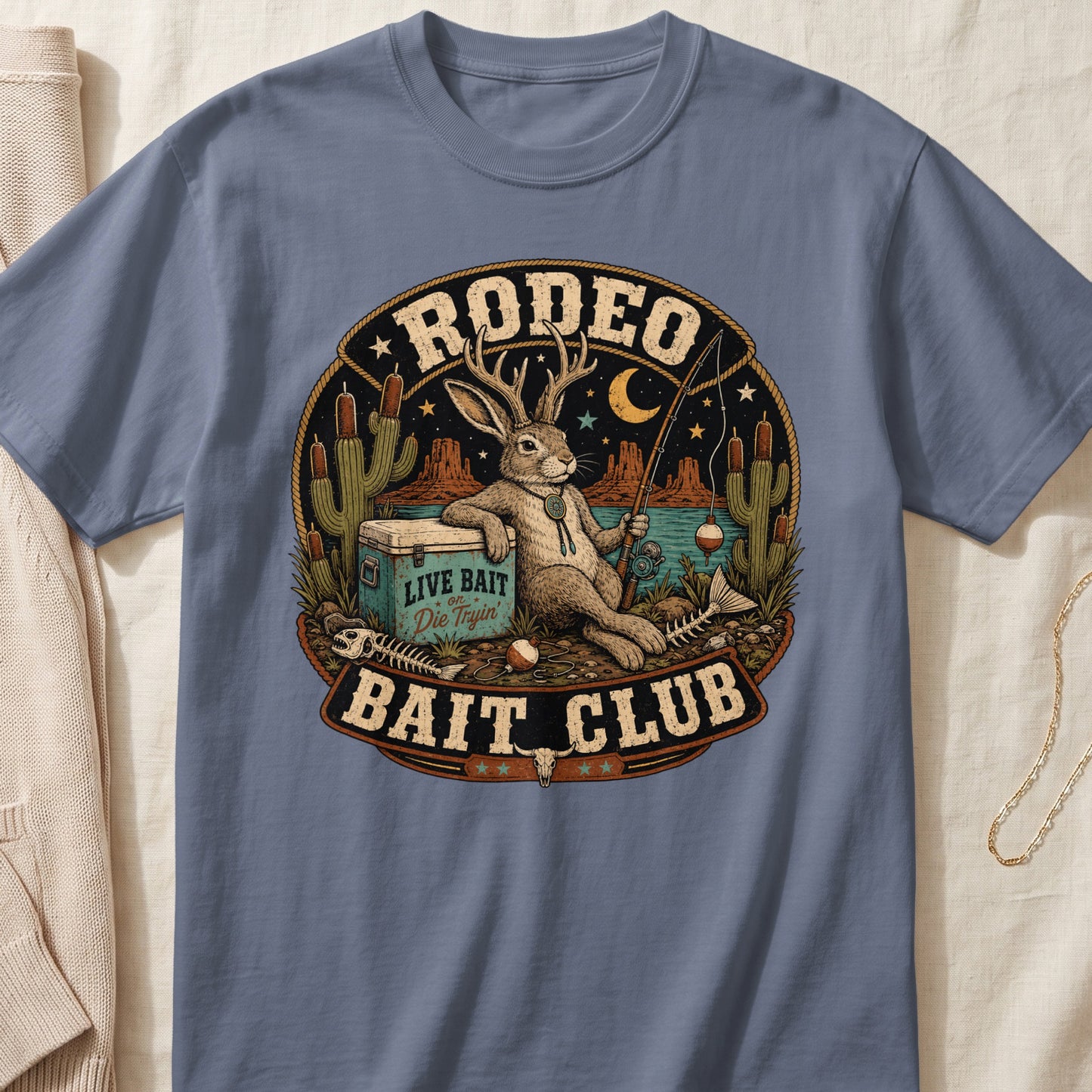 Rodeo Bait Club graphic on a blue t-shirt featuring a jackalope fishing and a cooler.