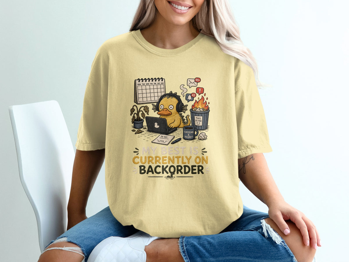 Yellow t-shirt with cartoon duck, laptop, calendar, and text "MY BEST IS CURRENTLY ON BACKORDER".