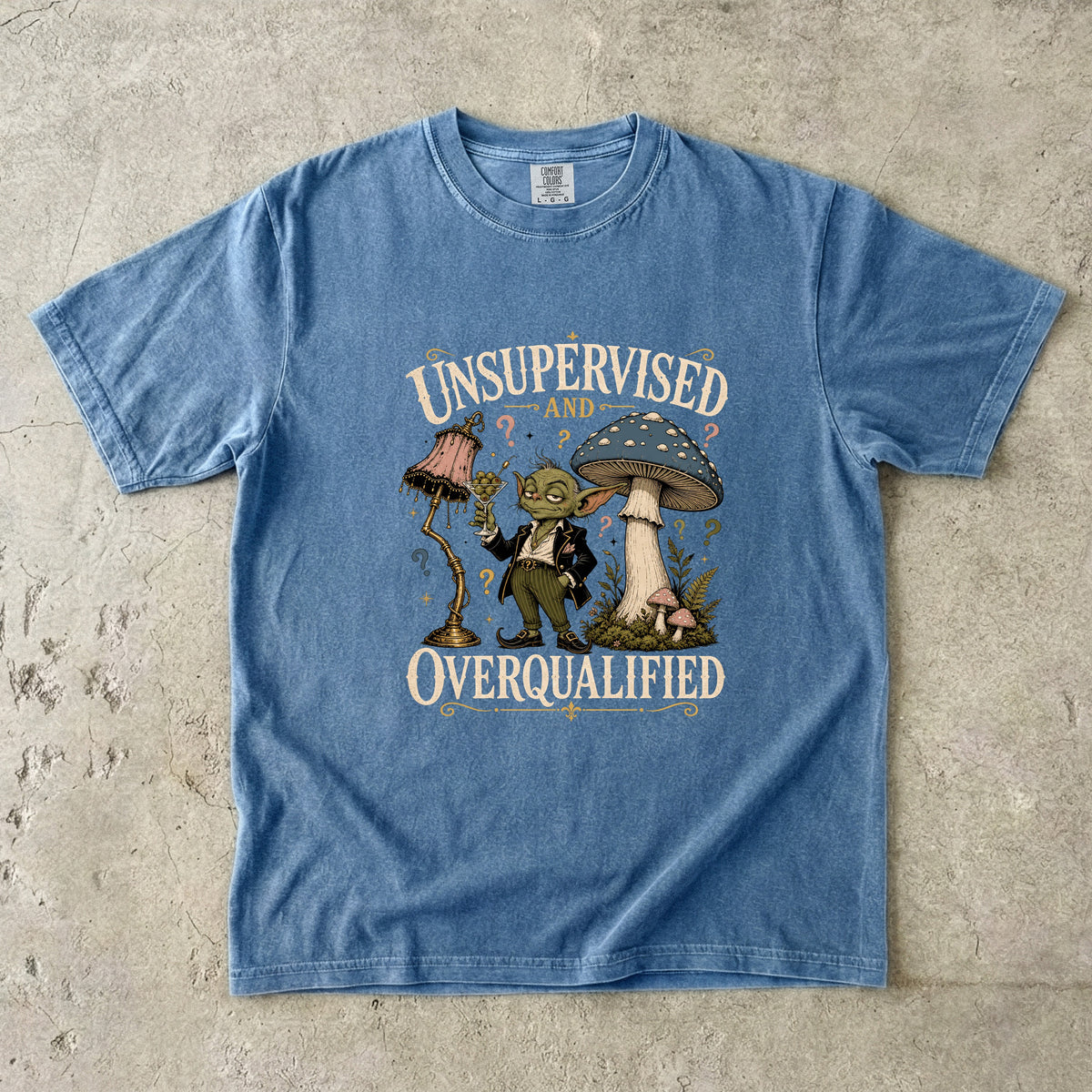 Blue t-shirt graphic of a goblin with a lamp and mushroom, text reads "UNSUPERVISED AND OVERQUALIFIED".