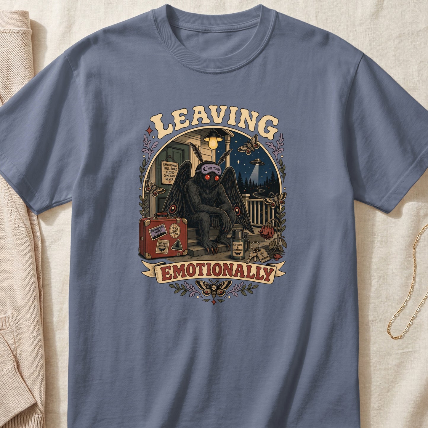 Graphic tee featuring a mothman sitting on steps with suitcase and signs.