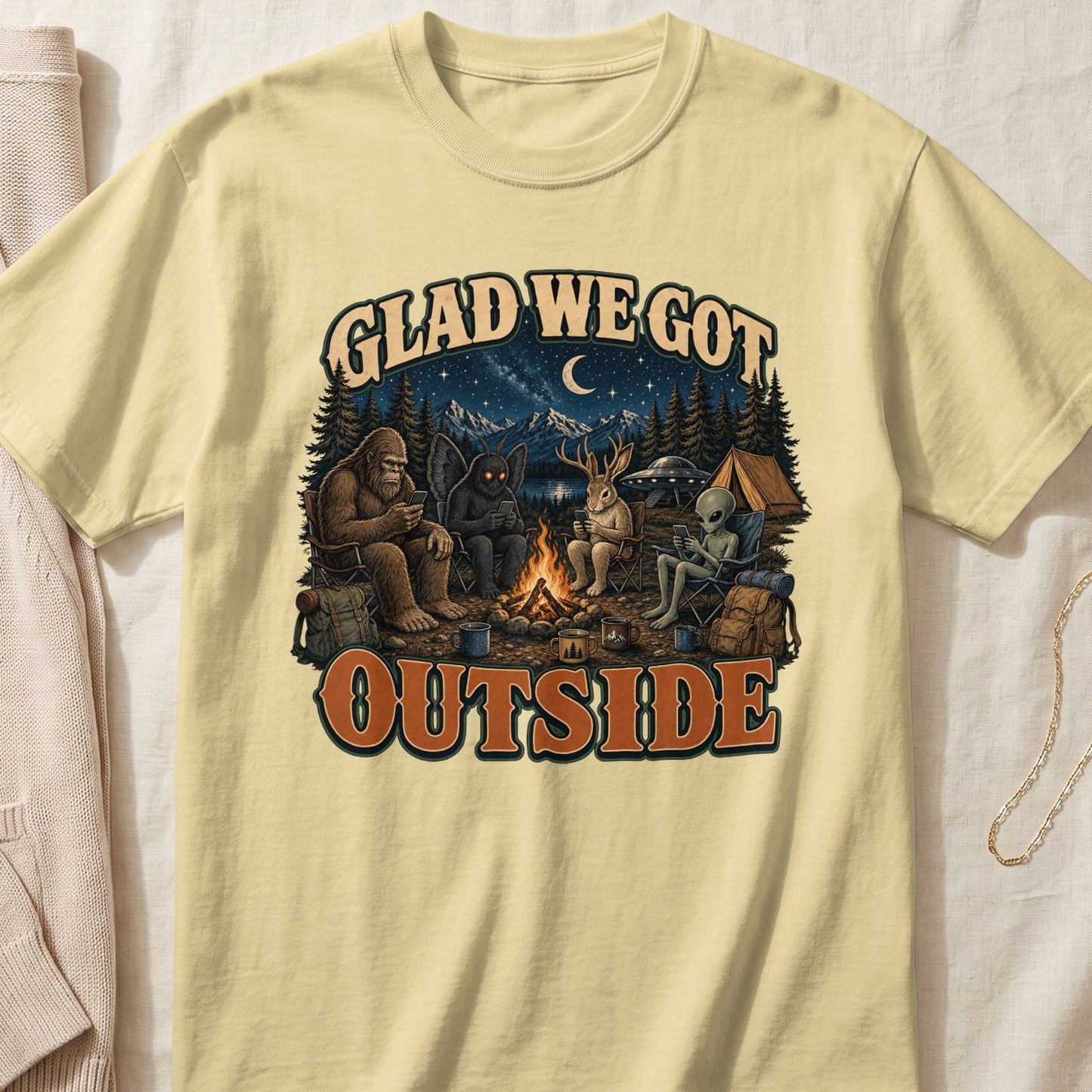 Bigfoot, Mothman, rabbit, and alien friends camp under a starry night sky.