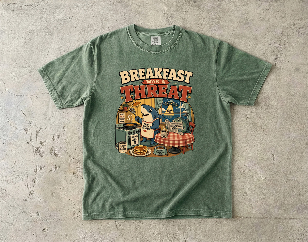 Green t-shirt with cartoon shark cooking breakfast and text "Breakfast Was A Threat."