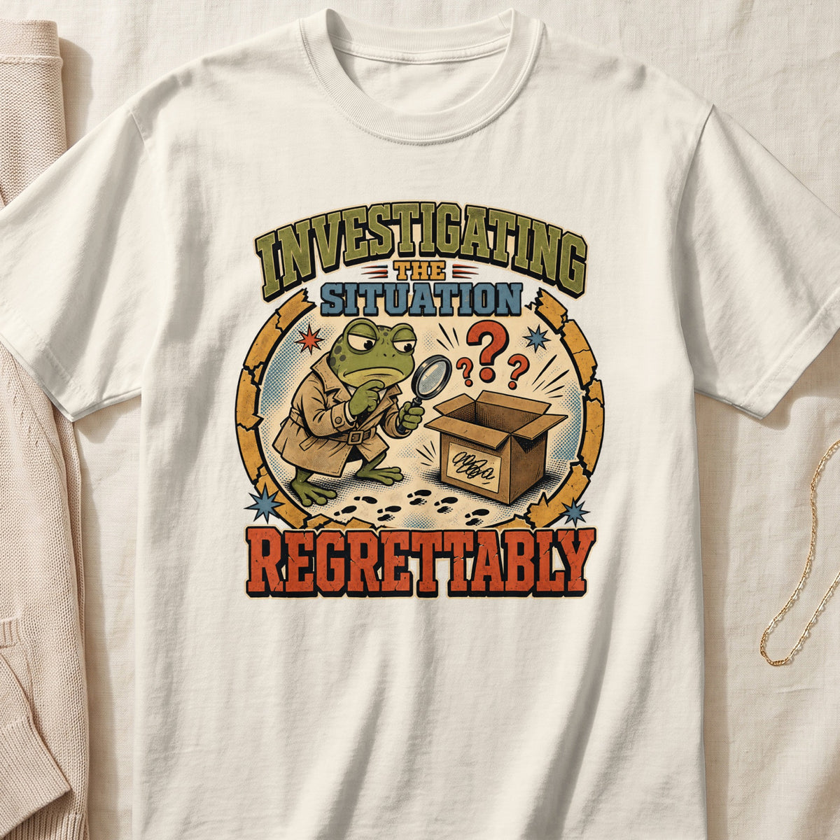 Off-white t-shirt featuring a vintage cartoon graphic of a frog detective investigating an empty cardboard box.
