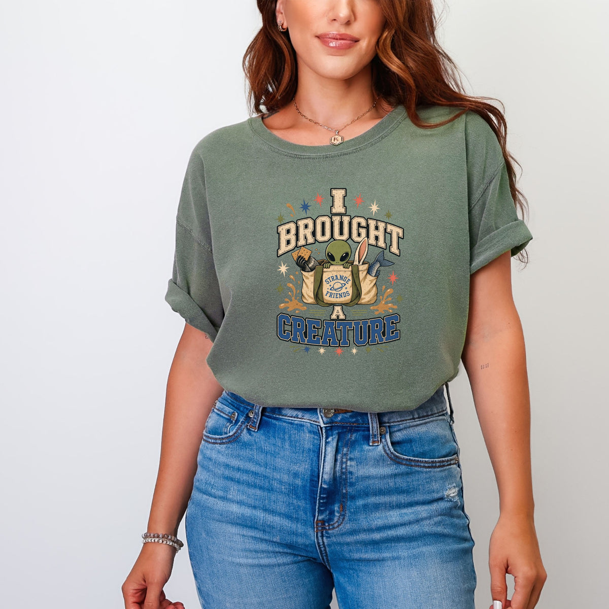 Green t-shirt with a graphic of an alien and items in a bag that says "Strange Friends".