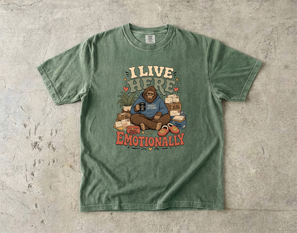 Green t-shirt with graphic of Bigfoot holding mug and text "I LIVE HERE EMOTIONALLY".