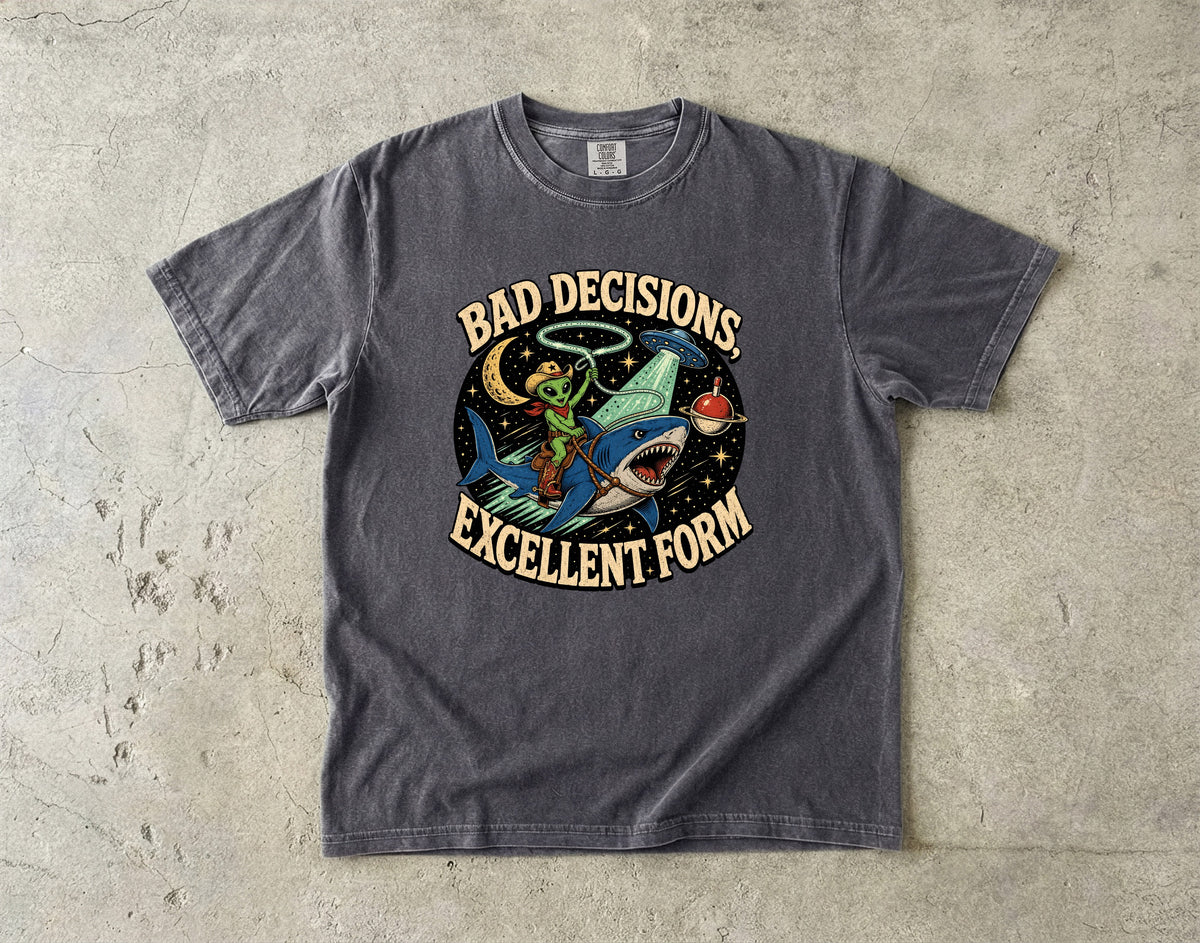 T-shirt graphic with alien cowboy riding a shark under a UFO and moon.
