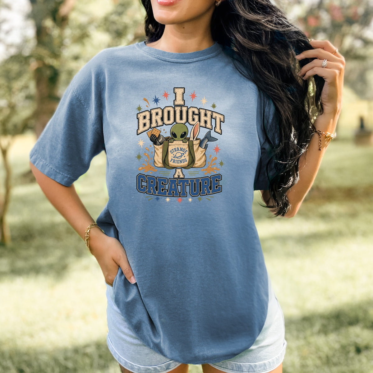Blue t-shirt graphic with text "I BROUGHT STRANGE FRIENDS A CREATURE" and alien.