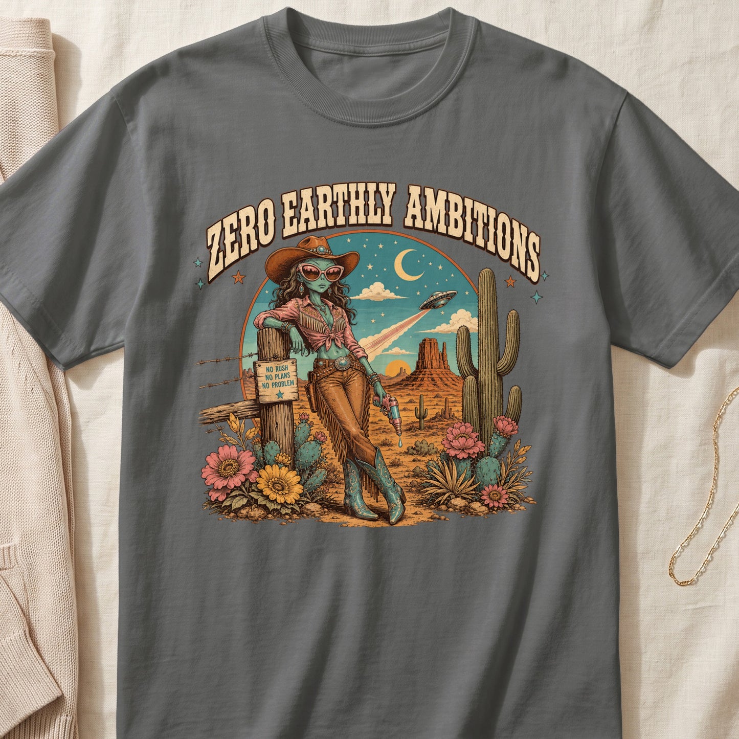 Graphic tee with alien in cowboy hat and desert scene, text "ZERO EARTHLY AMBITIONS".