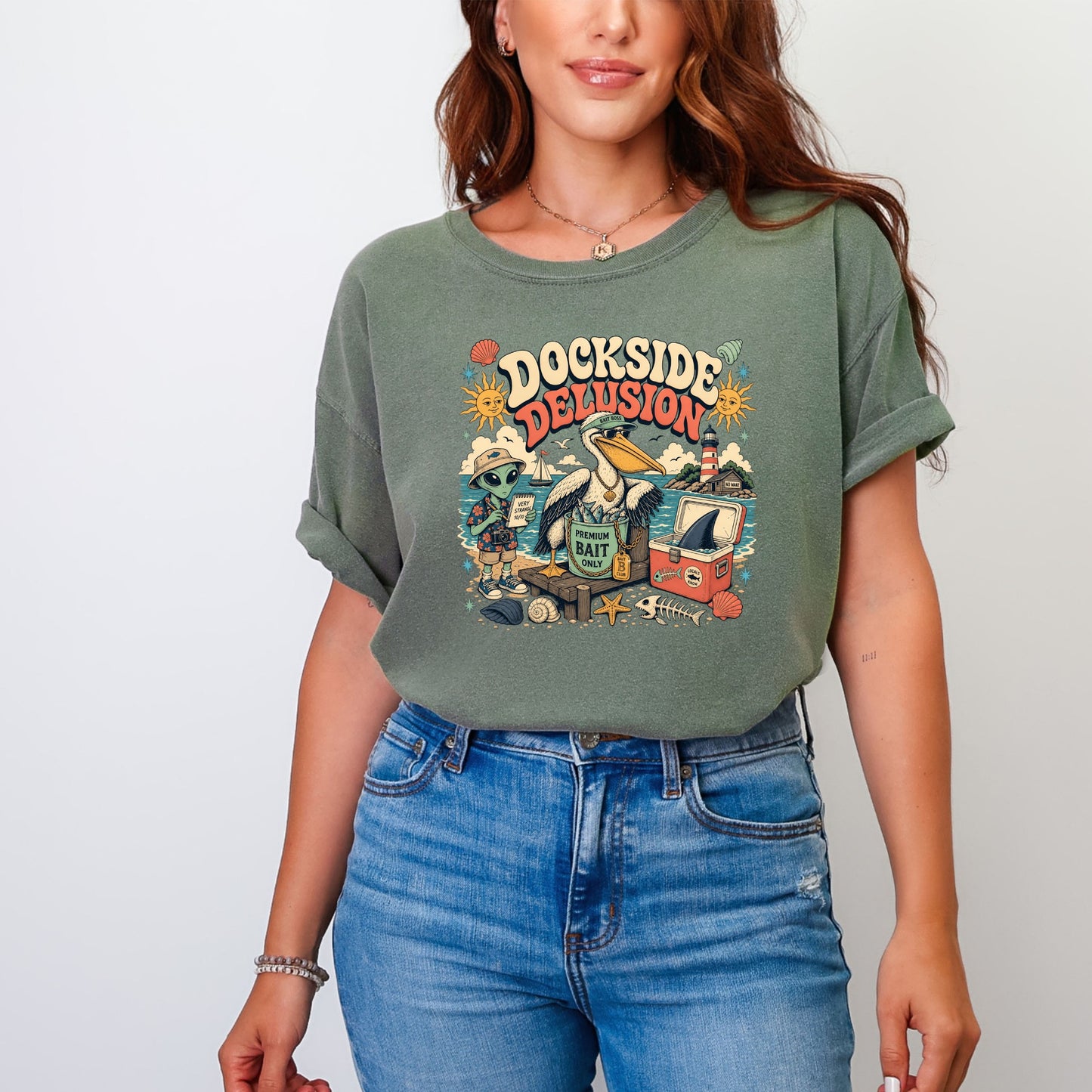 Green t-shirt with "DOCKSIDE DELUSION" text and cartoon aliens, pelican, and beach scene.