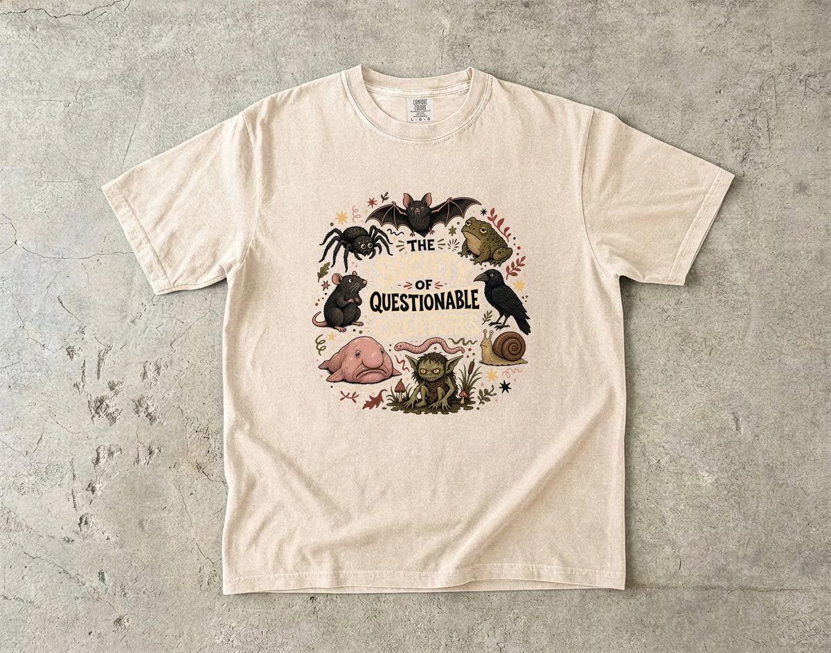T-shirt graphic with a bat, spider, frog, crow, and other creatures forming a circle around text.