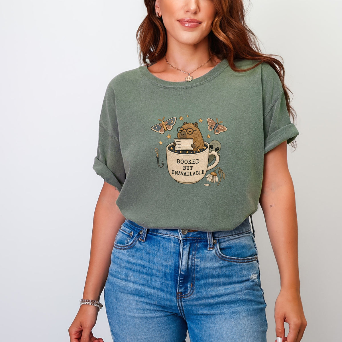 T-shirt graphic with a mug, a beaver reading, butterflies, and "Booked but Unavailable" text.