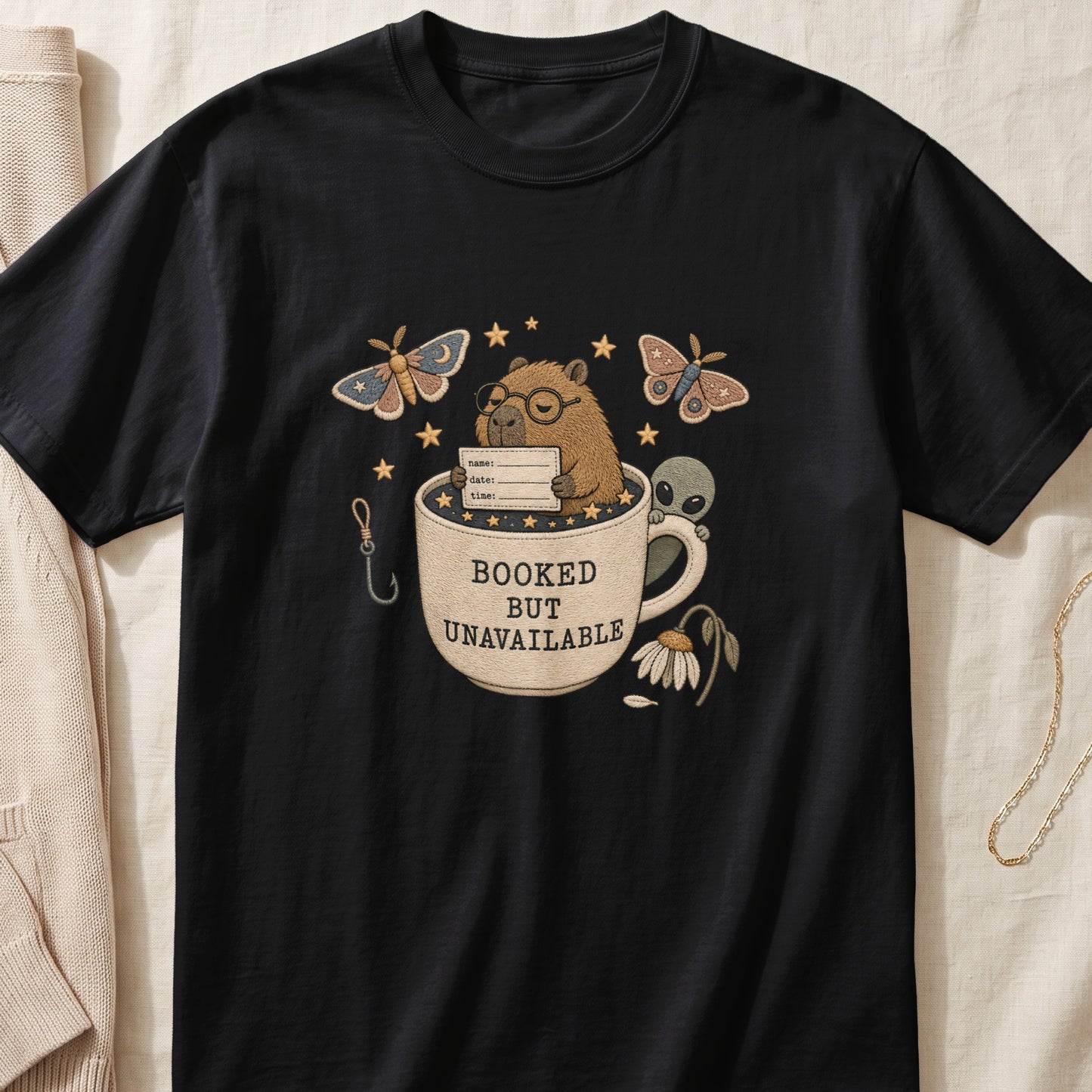 Black t-shirt with embroidered design of a capybara in a mug with alien and moths.