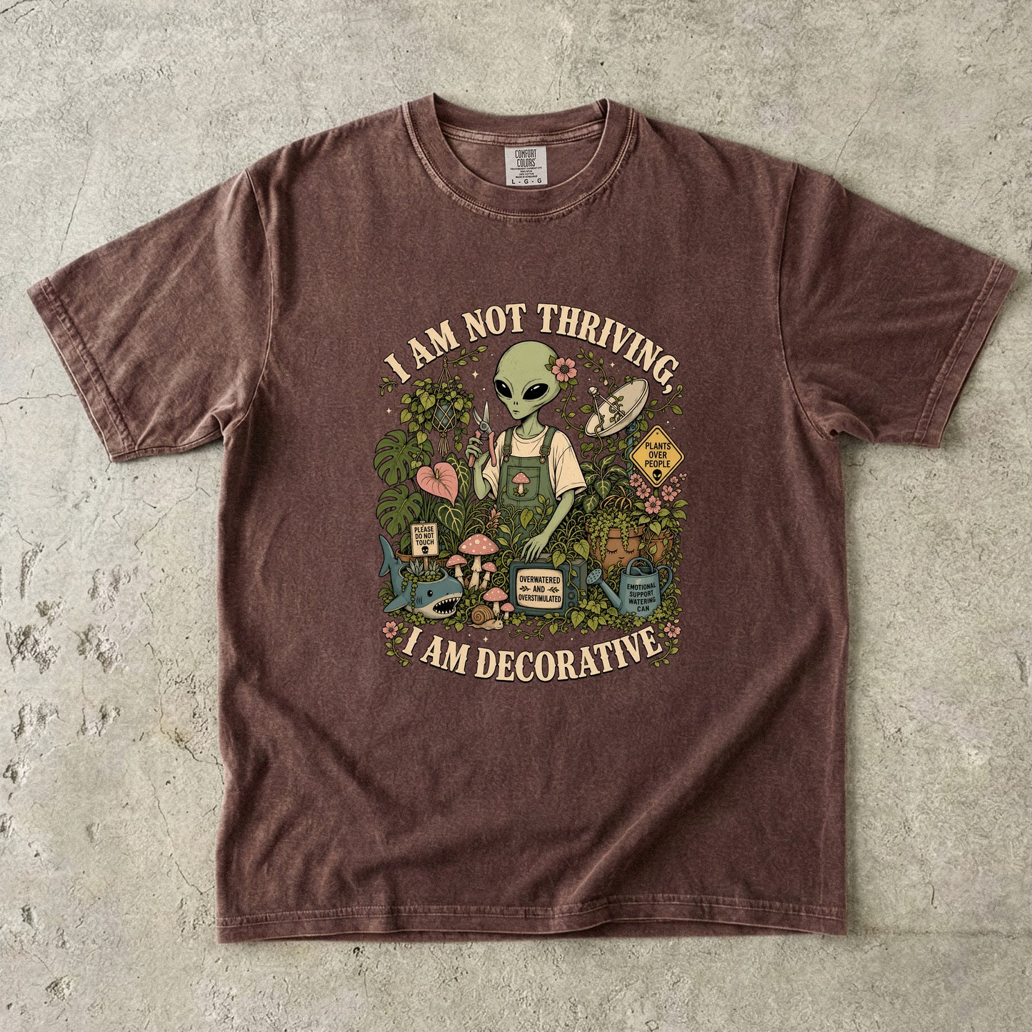 Brown t-shirt graphic with alien, plants, and text "I AM NOT THRIVING, I AM DECORATIVE".
