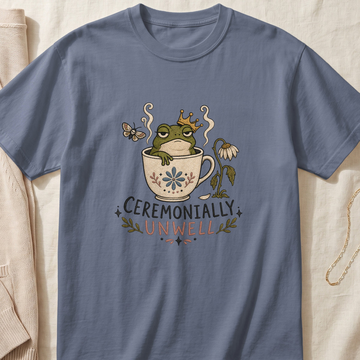T-shirt with illustration of crowned frog in teacup with text "CEREMONIAILY UNWELL".