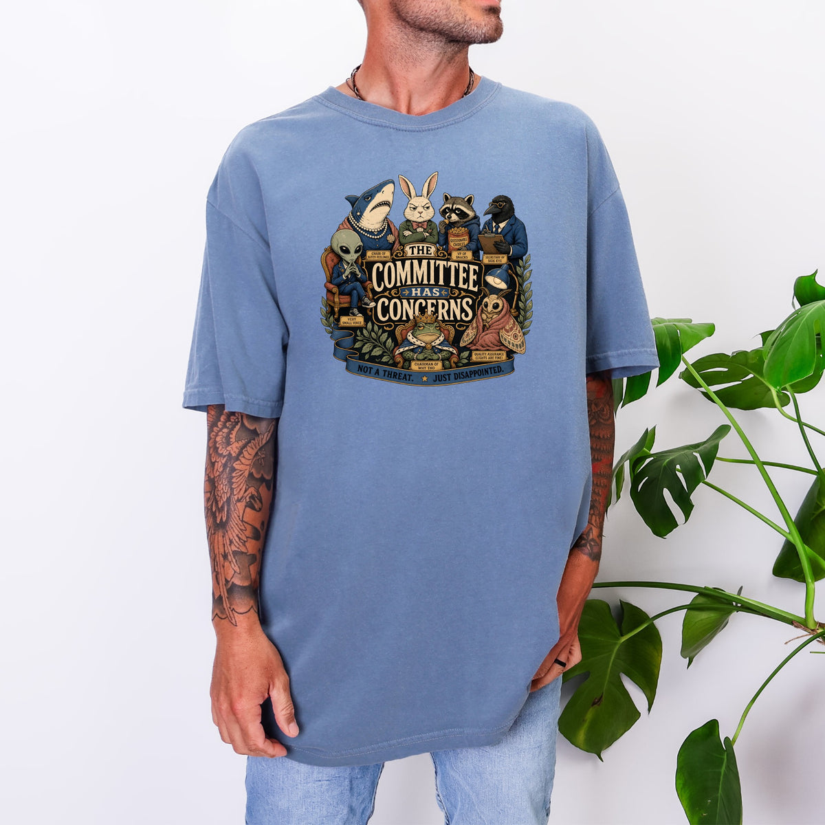 A man wearing a blue oversized t-shirt printed with anthropomorphic animals titled The Committee Has Concerns.