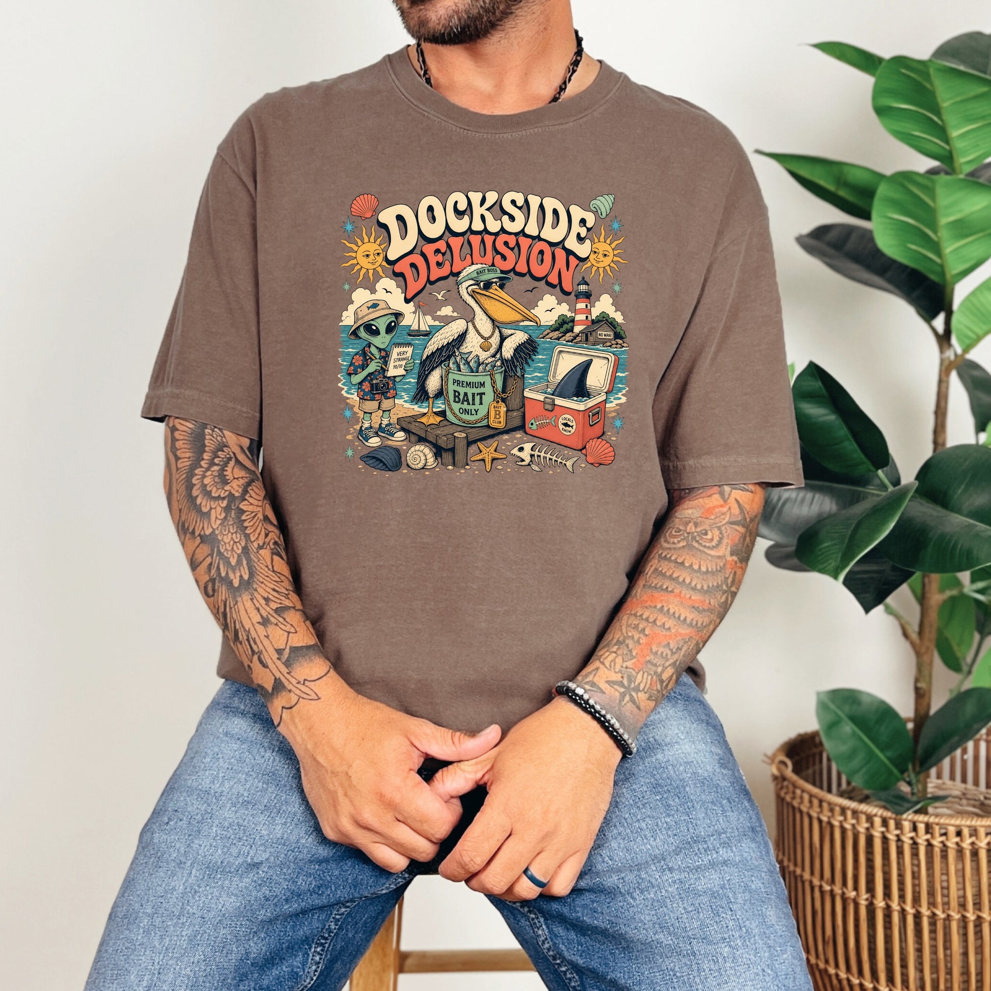 Shirt graphic: Dockside Delusion with alien, pelican, lighthouse, and fishing gear.