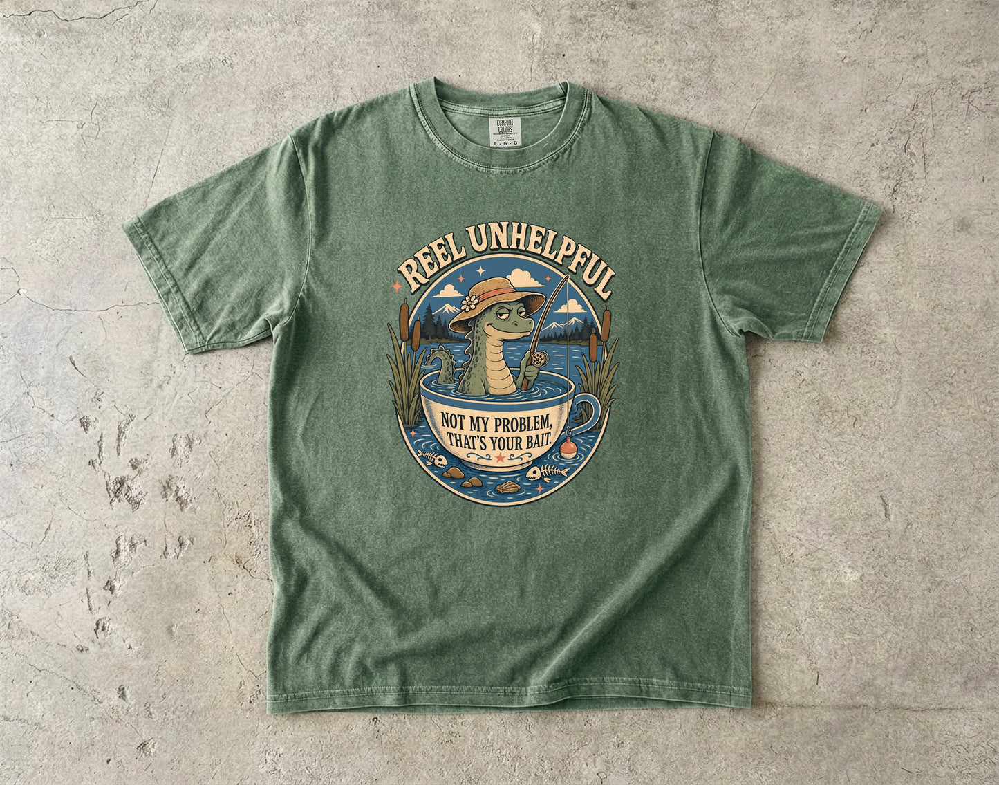 Green t-shirt with a graphic of a crocodile fishing and text "REEL UNHELPFUL NOT MY PROBLEM, THAT'S YOUR BAIT."