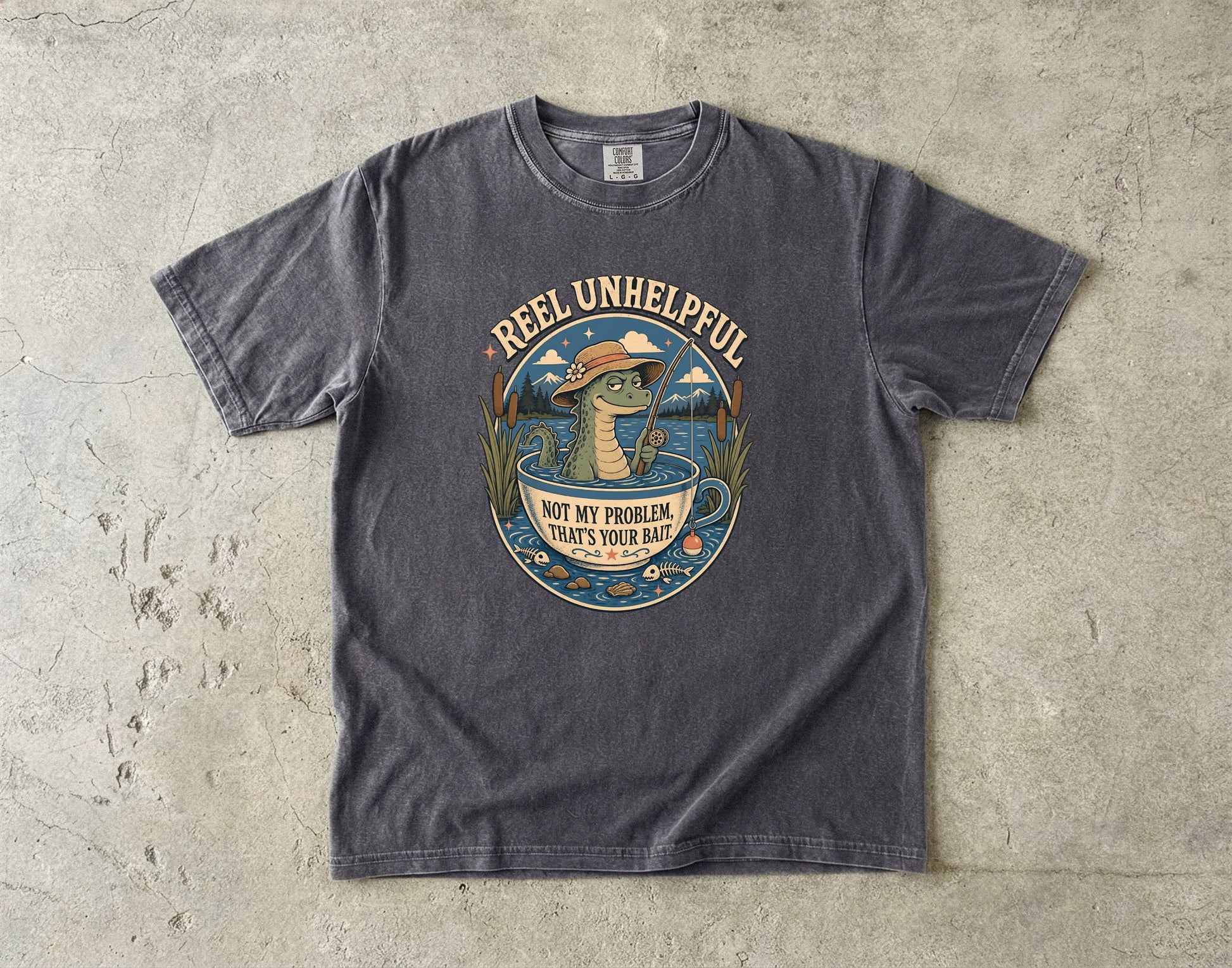 Dark grey t-shirt with graphic of a dinosaur fishing in a teacup, text reads "REEL UNHELPFUL NOT MY PROBLEM, THAT'S YOUR BAIT".