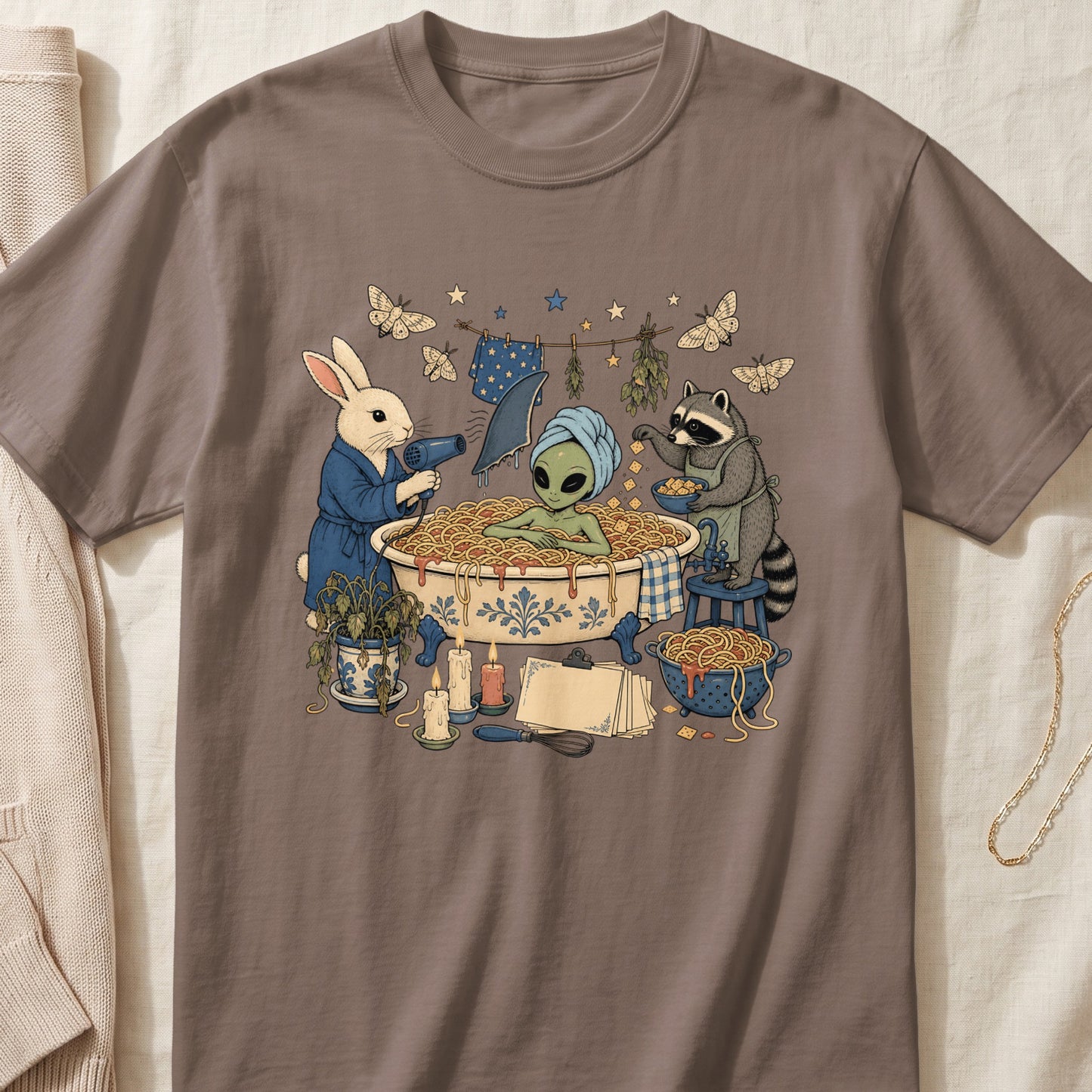 Brown t-shirt featuring an illustration of an alien in a spaghetti bath, assisted by a rabbit and raccoon.