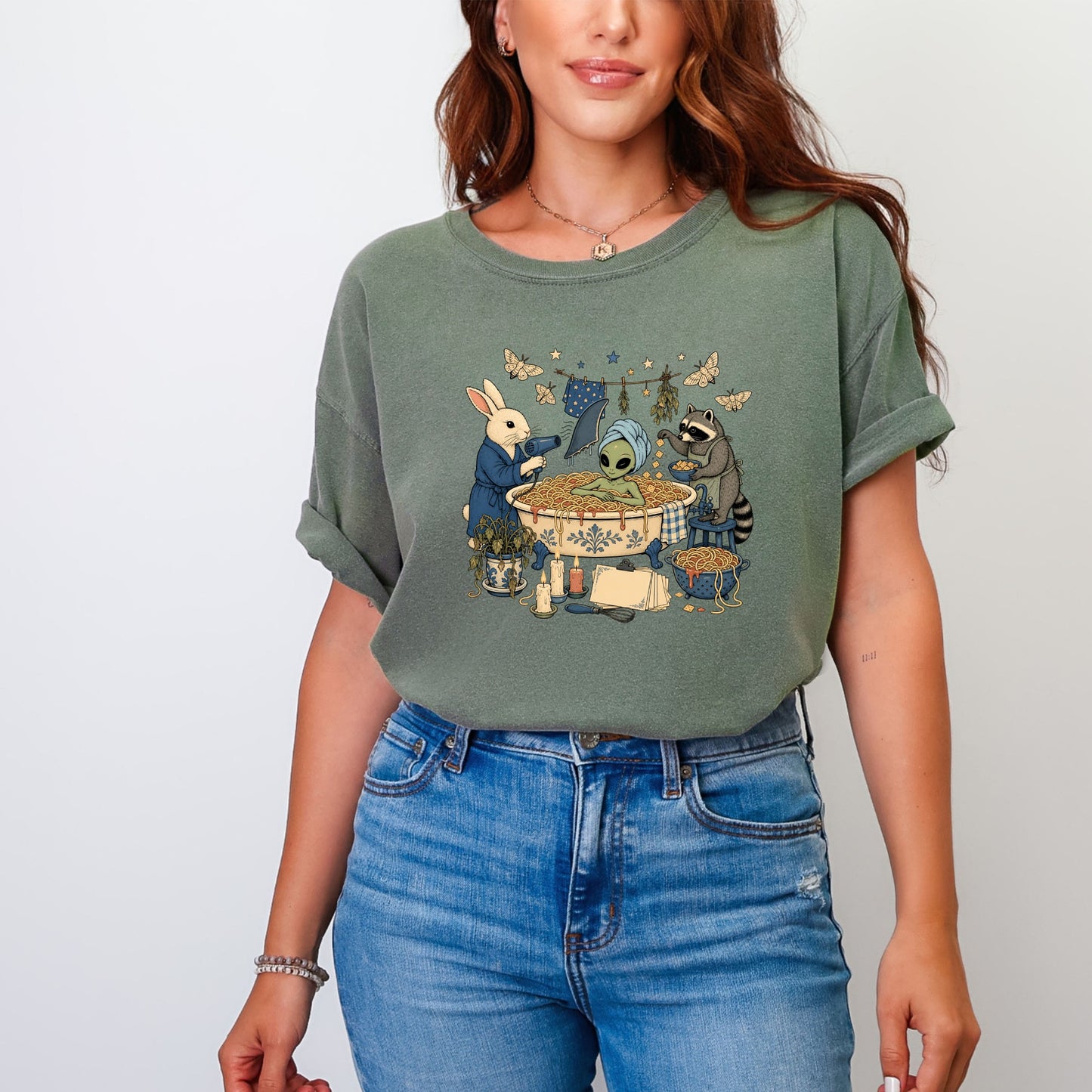 A woman wearing an olive-green t-shirt printed with an illustration of an alien bathing in spaghetti.