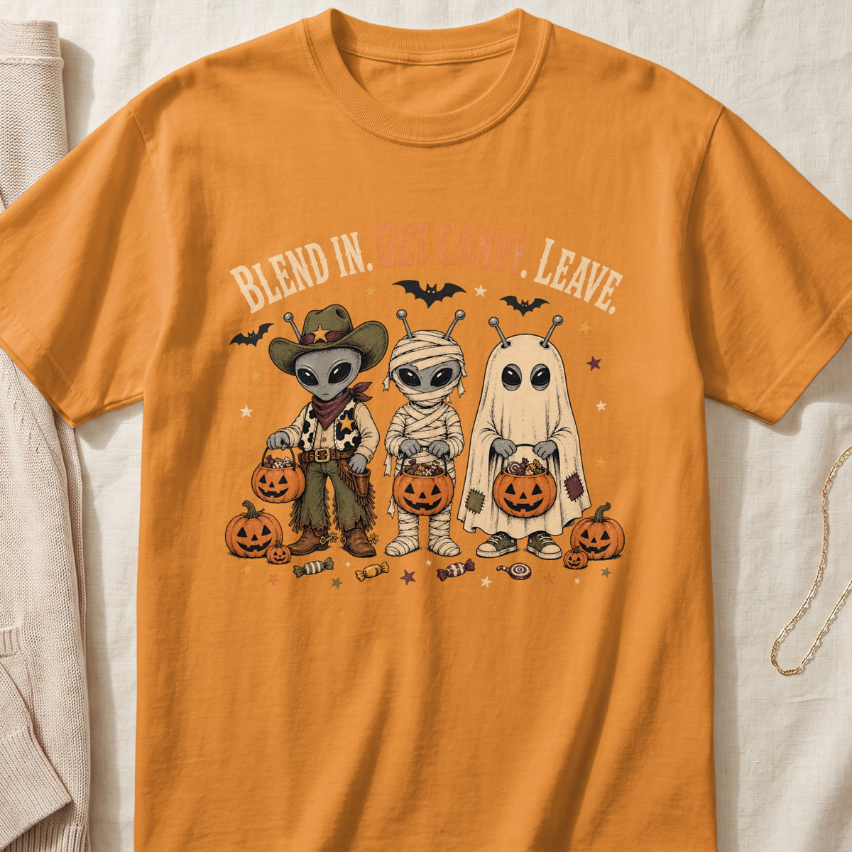 Orange t-shirt with aliens dressed as cowboy, mummy, and ghost for Halloween.