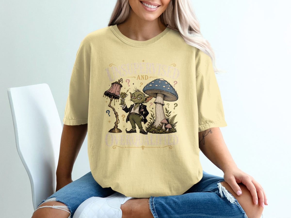 Graphic tee with whimsical art of a creature, mushroom, and lamp with text.