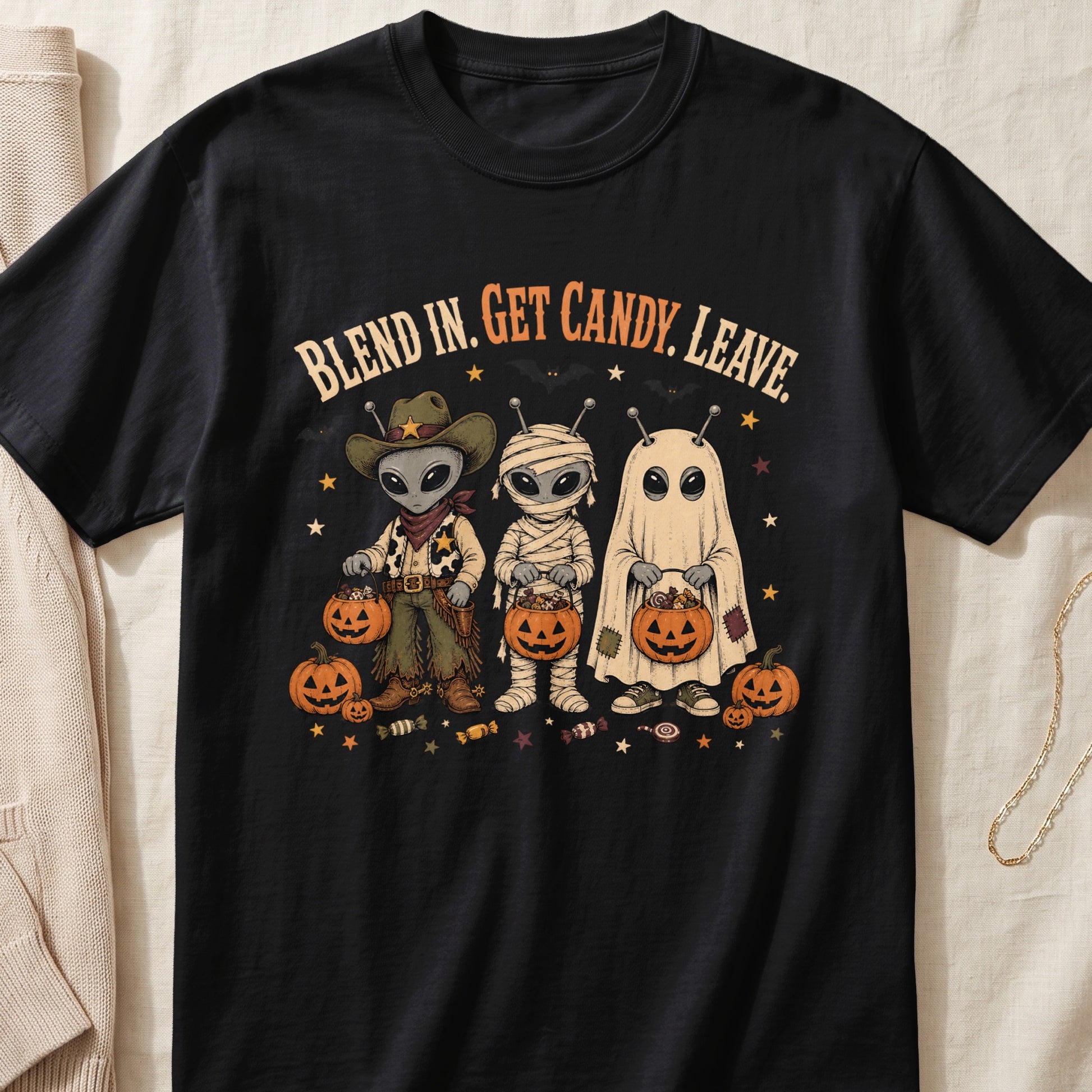 Black t-shirt with aliens dressed as a cowboy, mummy, and ghost holding candy pumpkins.