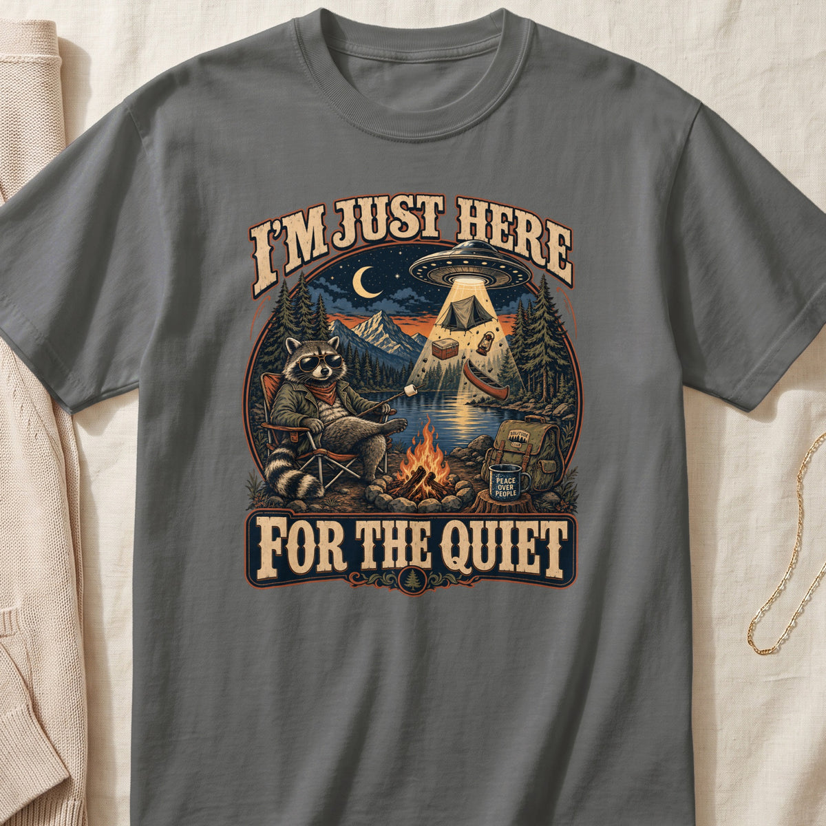 Raccoon sitting by campfire with UFO and text "I'M JUST HERE FOR THE QUIET"