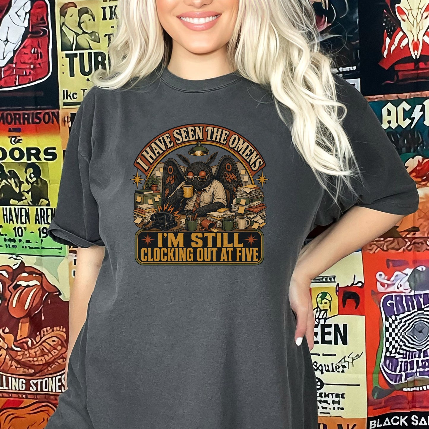 Dark t-shirt with moth-like creature at a desk with text "I HAVE SEEN THE OMENS I'M STILL CLOCKING OUT AT FIVE".