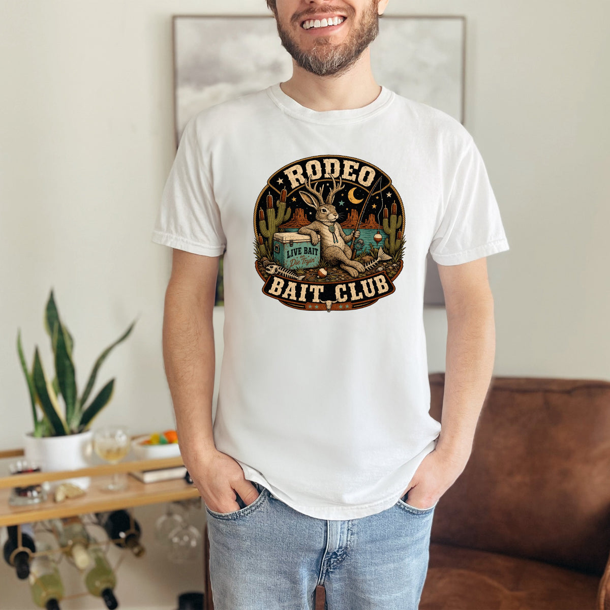 White t-shirt with "Rodeo Bait Club" graphic featuring a rabbit, fishing, and desert landscape.