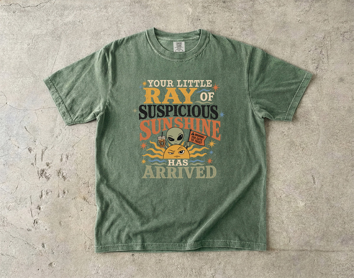 Green t-shirt with "Your little ray of suspicious sunshine has arrived" graphic.