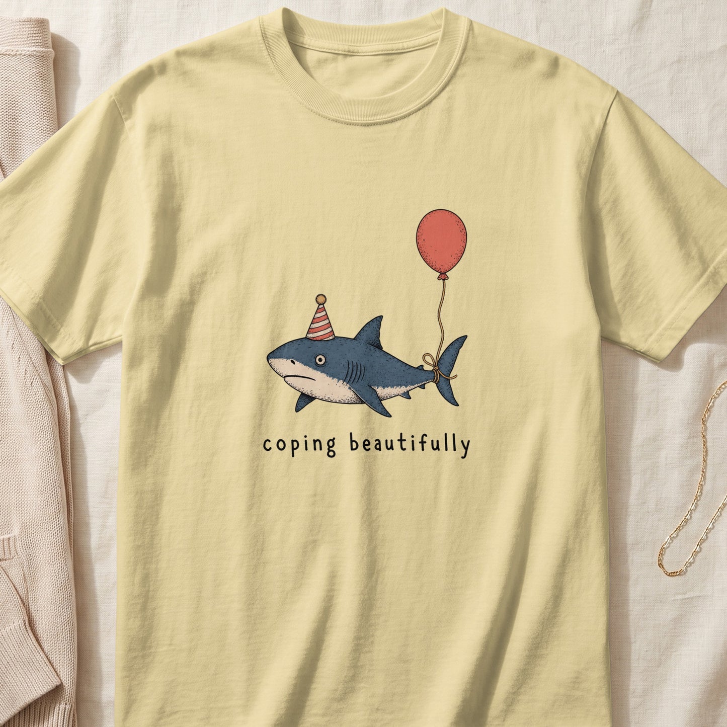 Shark wearing party hat holding balloon with text "coping beautifully"