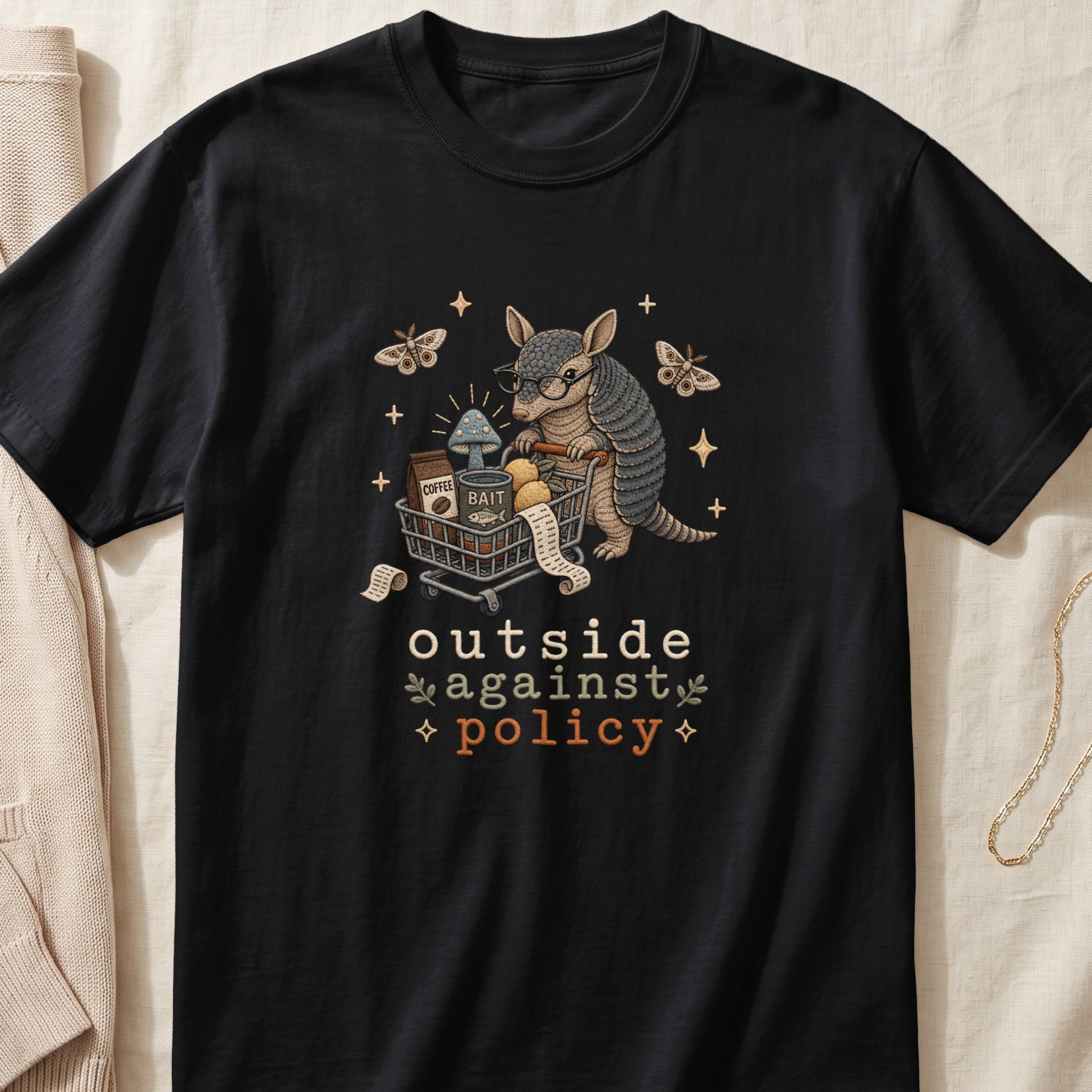 Black t-shirt with armadillo pushing shopping cart, featuring text "outside against policy".