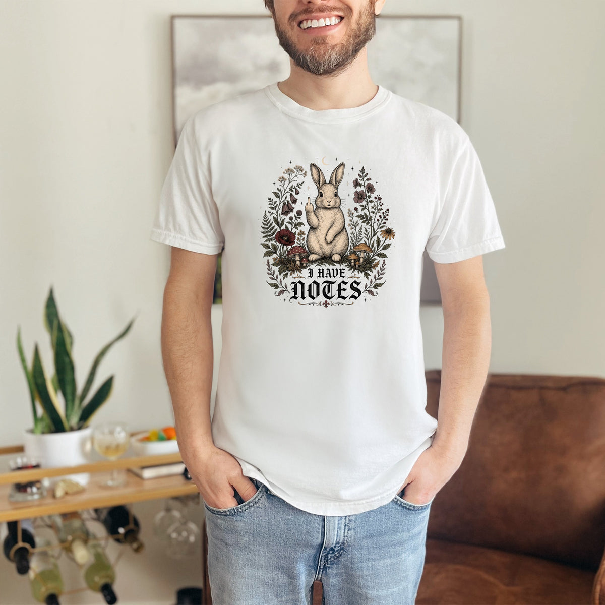 White t-shirt with illustration of bunny surrounded by flowers and mushrooms, text reads "I HAVE NOTES".