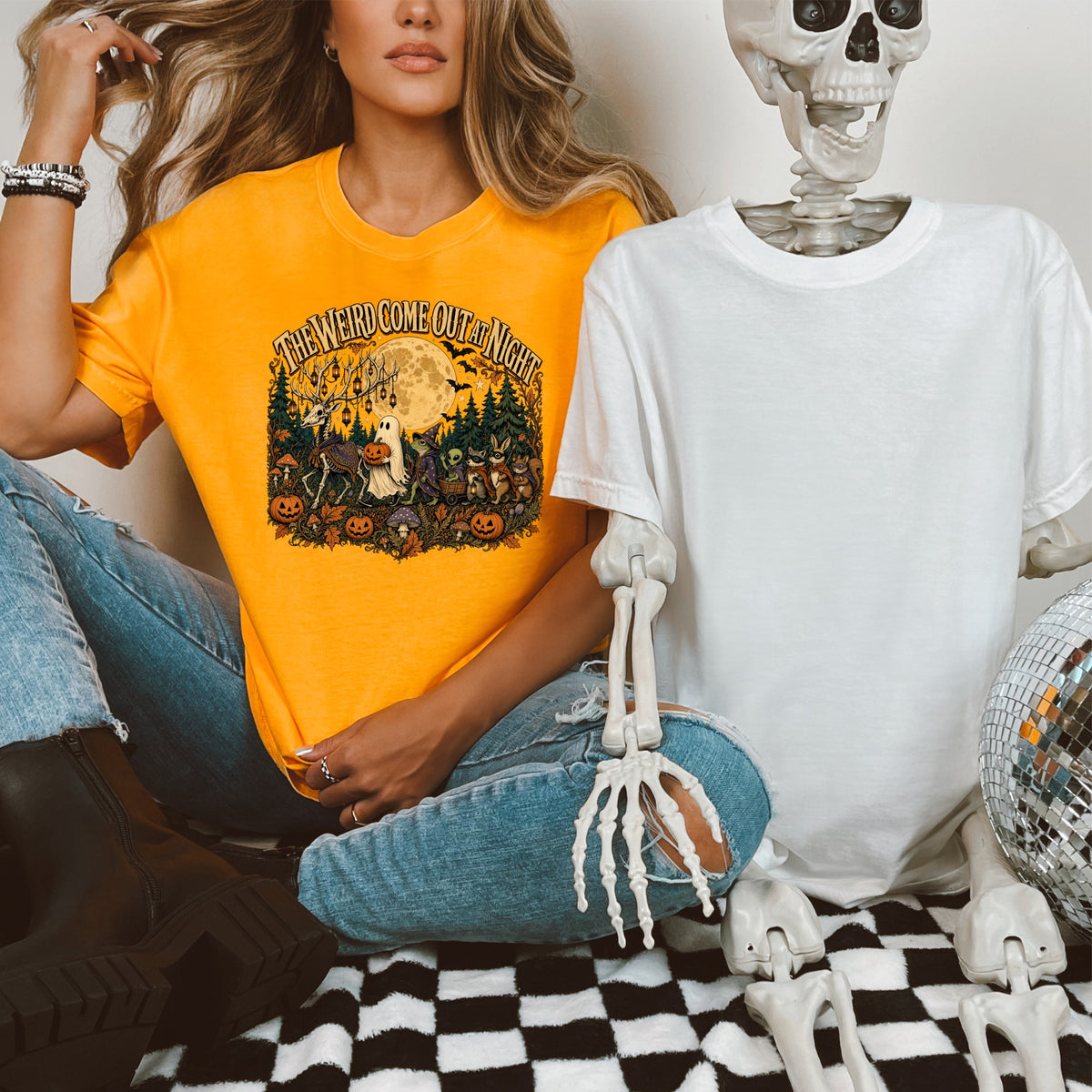 Orange t-shirt with "The Weird Come Out at Night" Halloween graphic, next to a white t-shirt and skeleton.