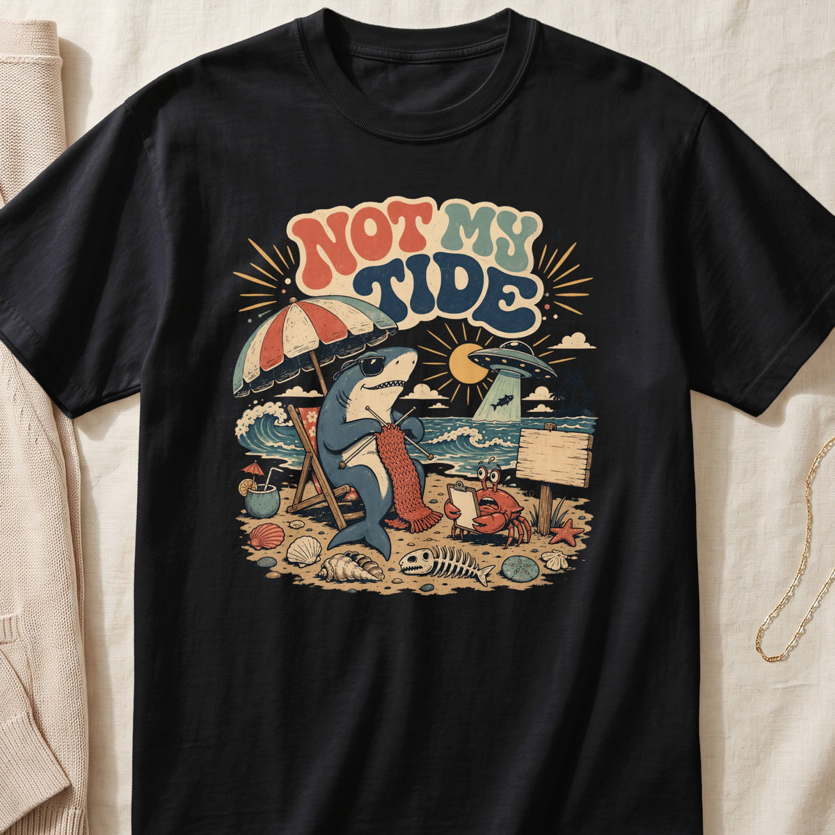 Shark knitting on a beach under a UFO with text "NOT MY TIDE."